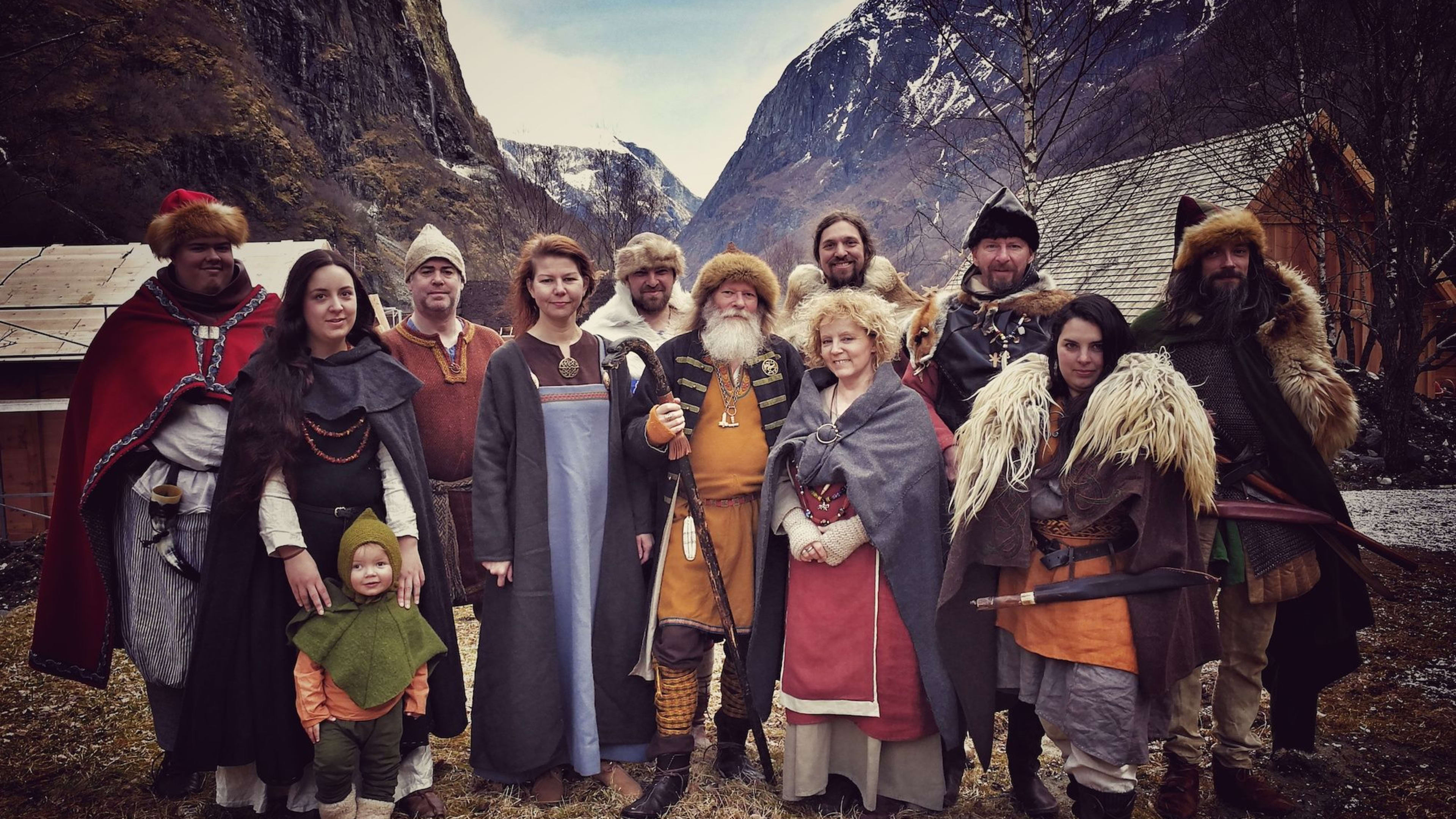 Group in Viking clothes poses in mountain valley with huts.