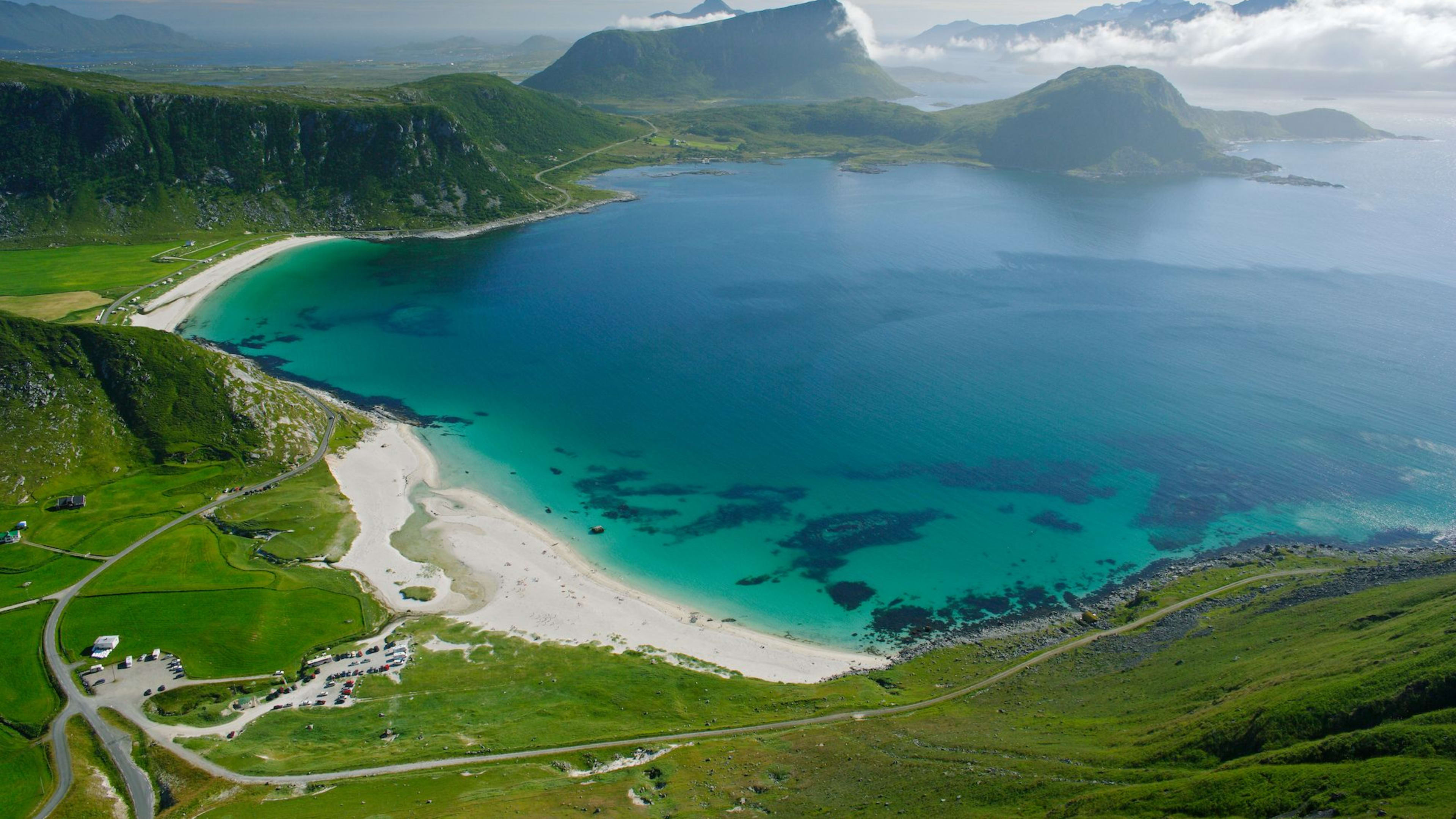 Eine atemberaubende Luftaufnahme von einer üppig grünen Landschaft, die zu einem unberührten weißen Sandstrand führt, umgeben von klarem türkisfarbenem Wasser.