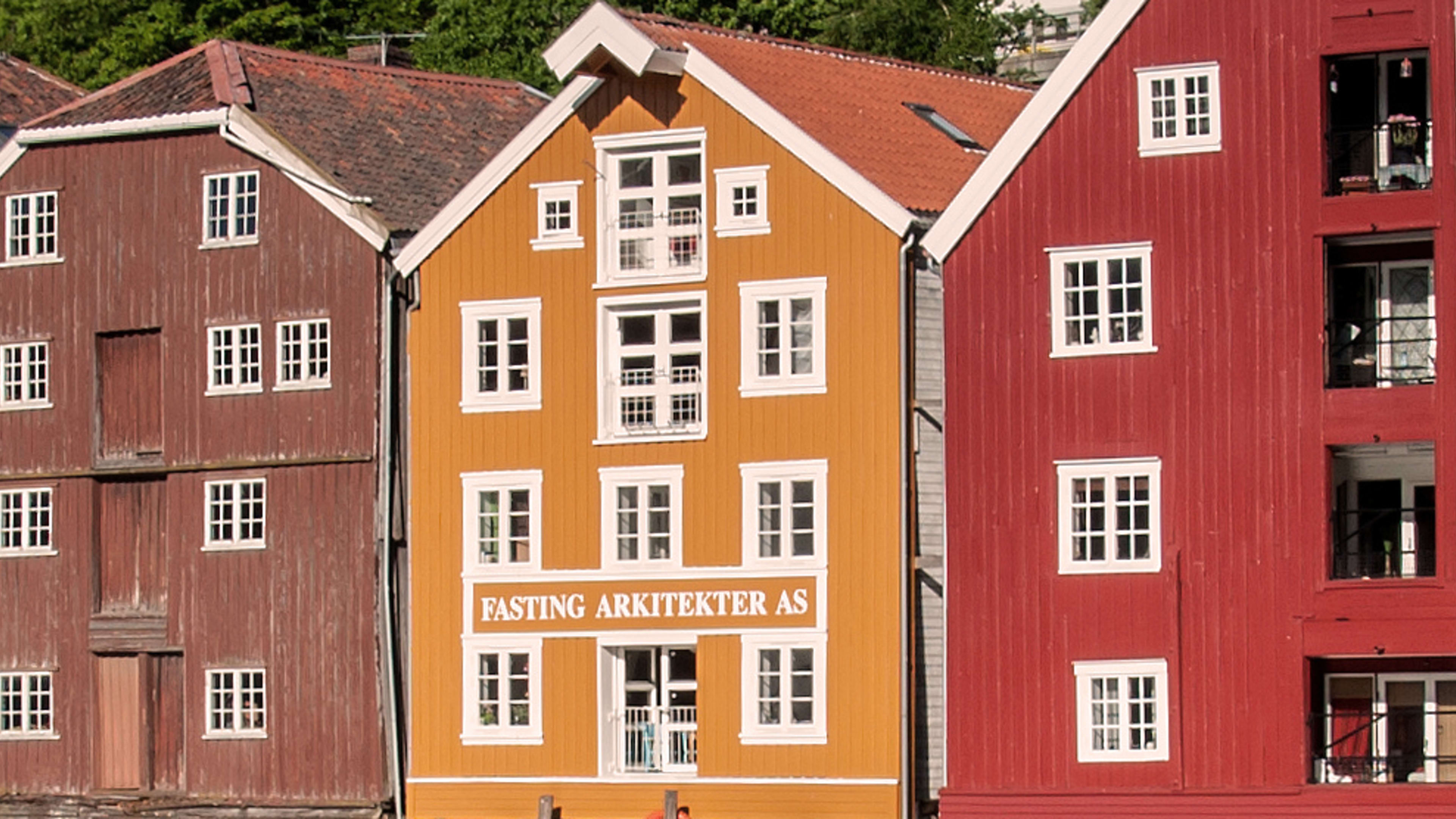 Colorful wooden houses along Nidelva river in Trondheim on sunny day with calm water reflections