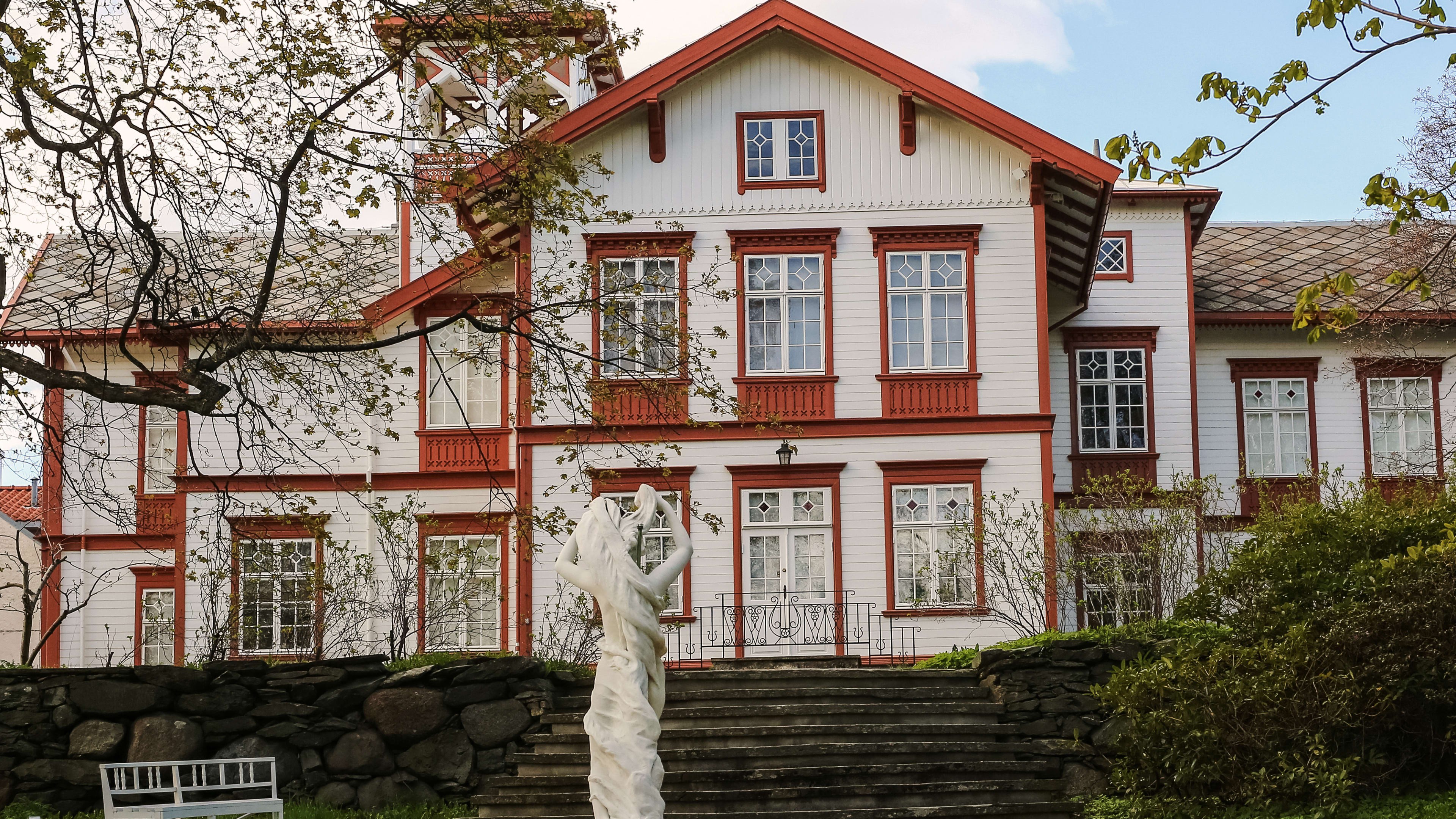 White historic manor building with garden, sculptures and flowering plants at Ringve Museum Trondheim