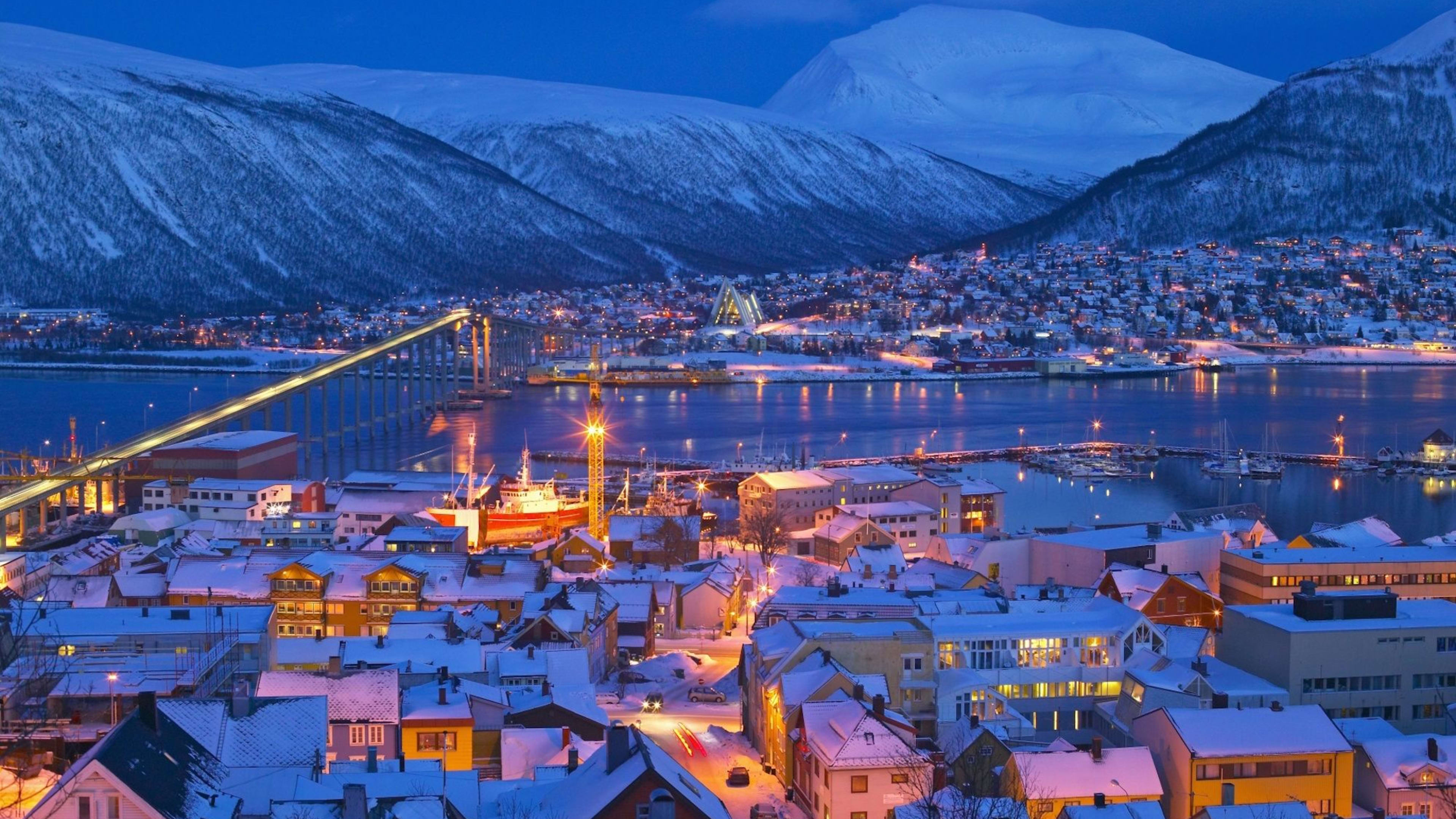 Tromsø winter city view with snow-covered roofs and glowing lights under blue Arctic sky