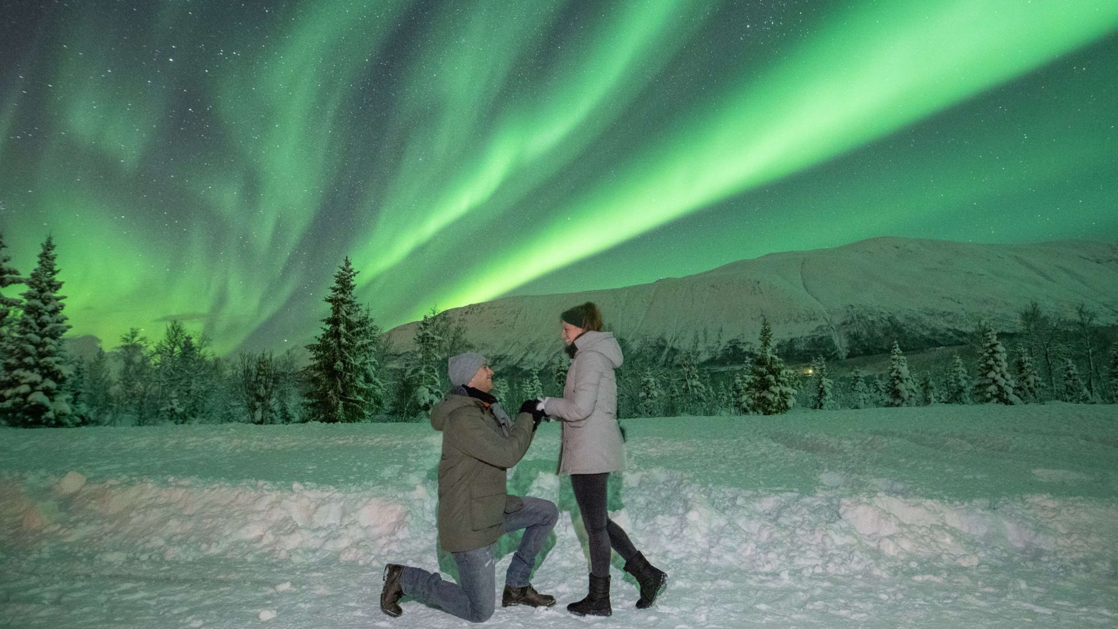 Romantische Winter-Szene mit einem Paar unter den Nordlichtern, einer macht einen Heiratsantrag im Schnee.