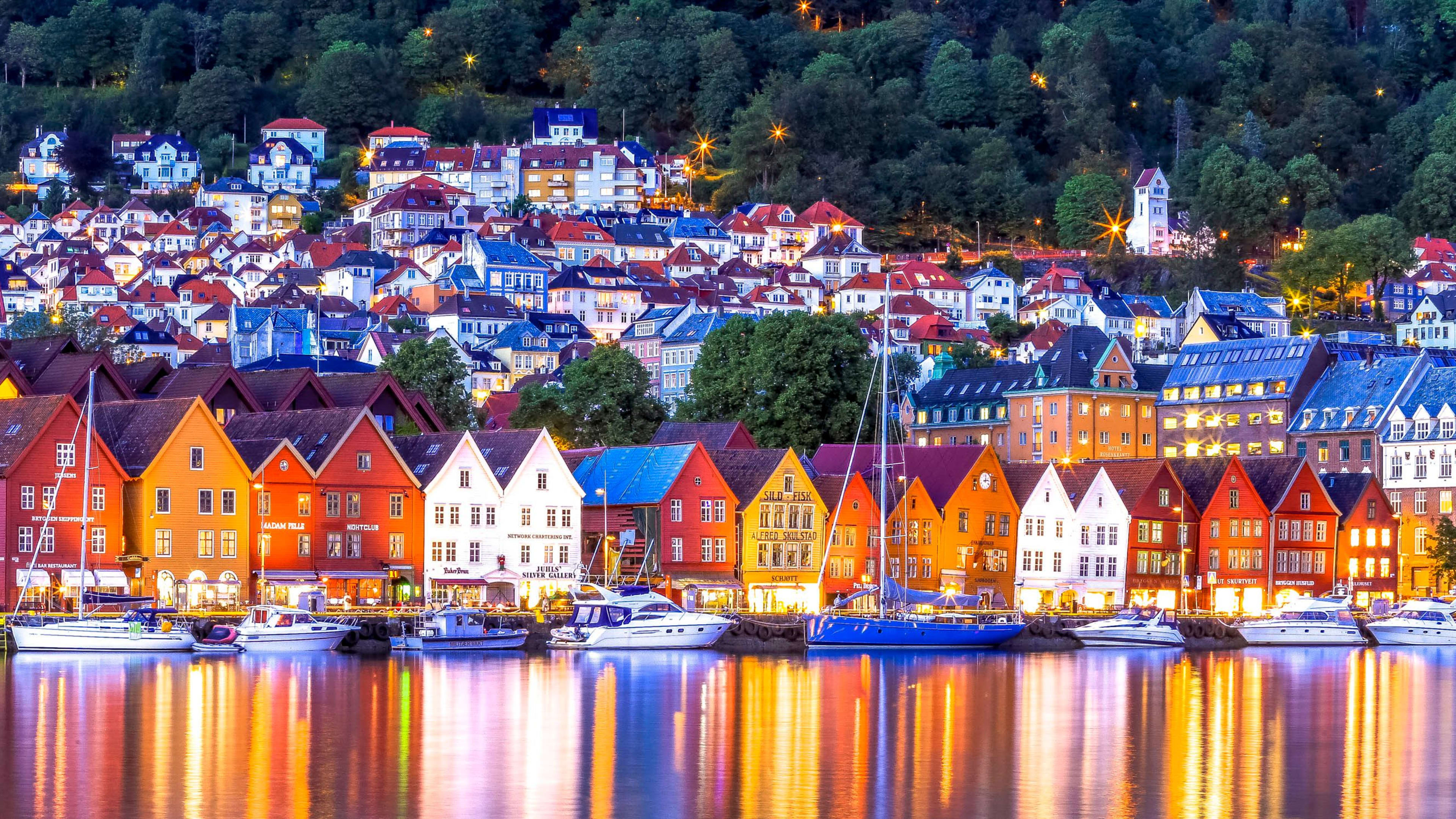 Dusk view of waterfront with boats and hillside town lights.