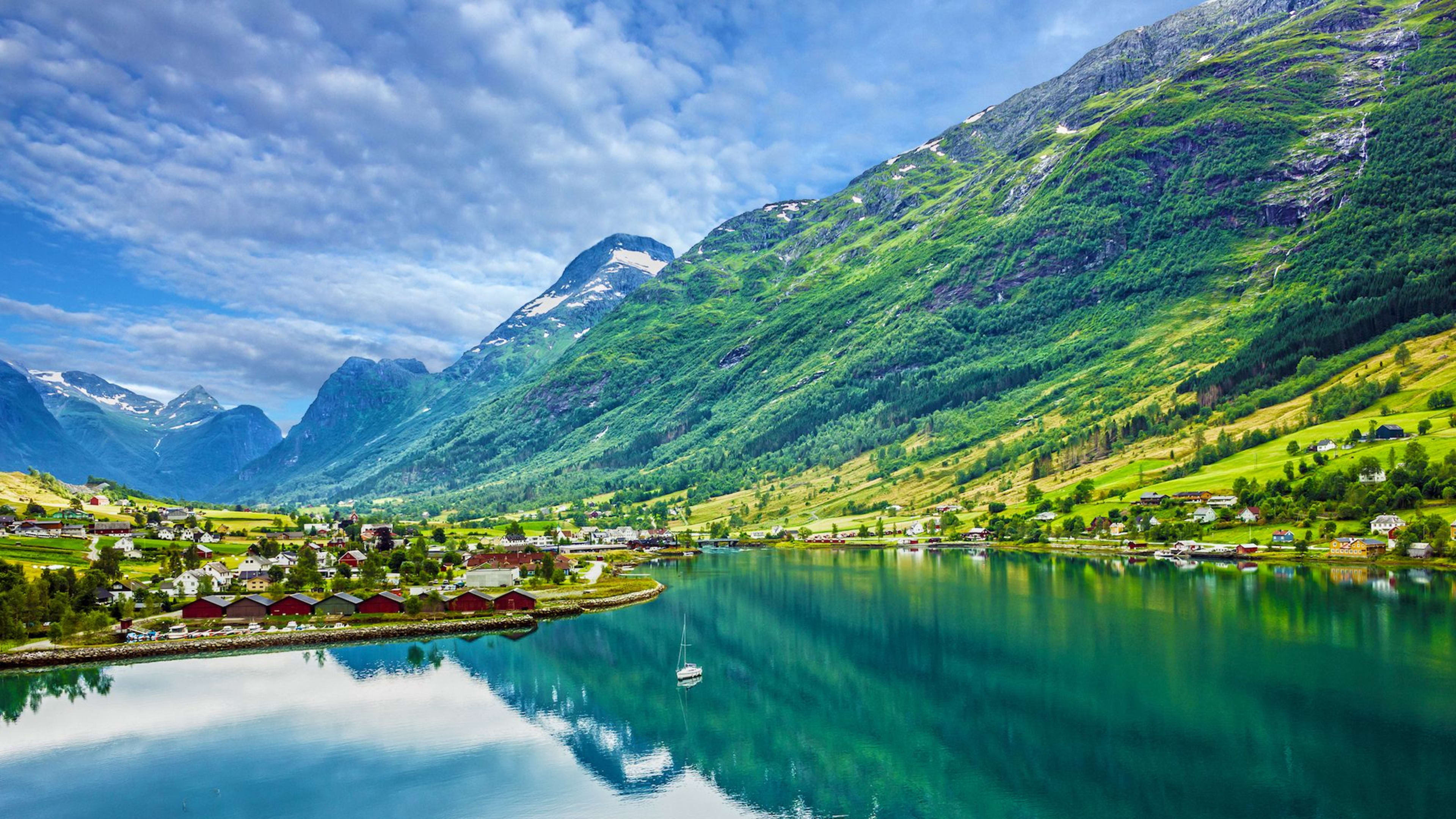 Ruhiges Fjorddorf mit Boot, Bergen und Spiegelung im Wasser.