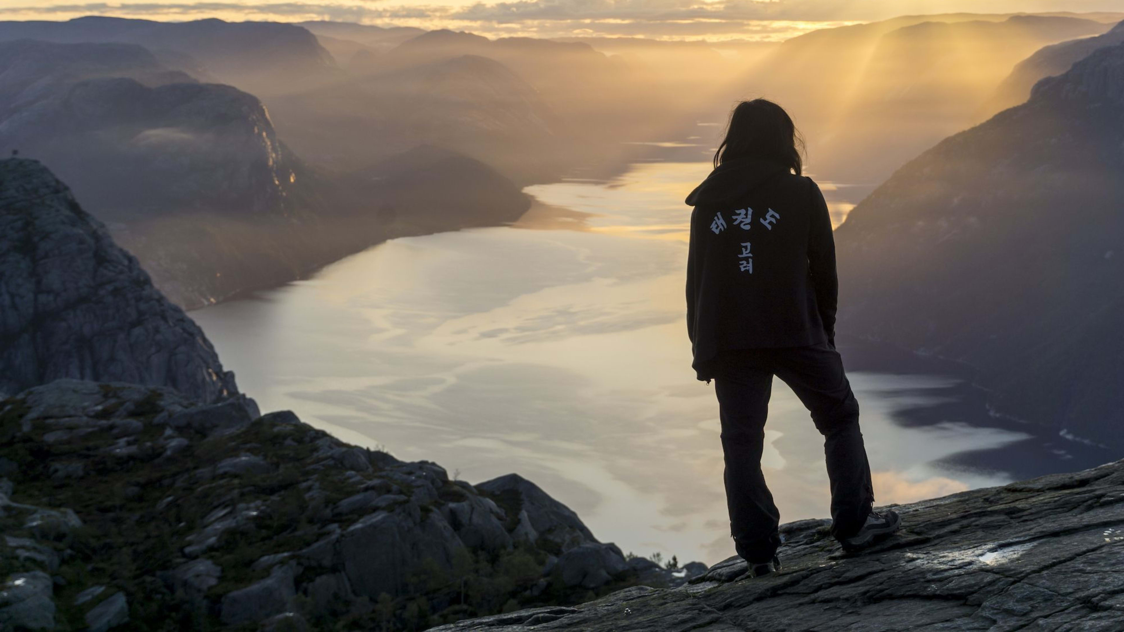 Person bei Sonnenaufgang überblickt nebligen Fjord.