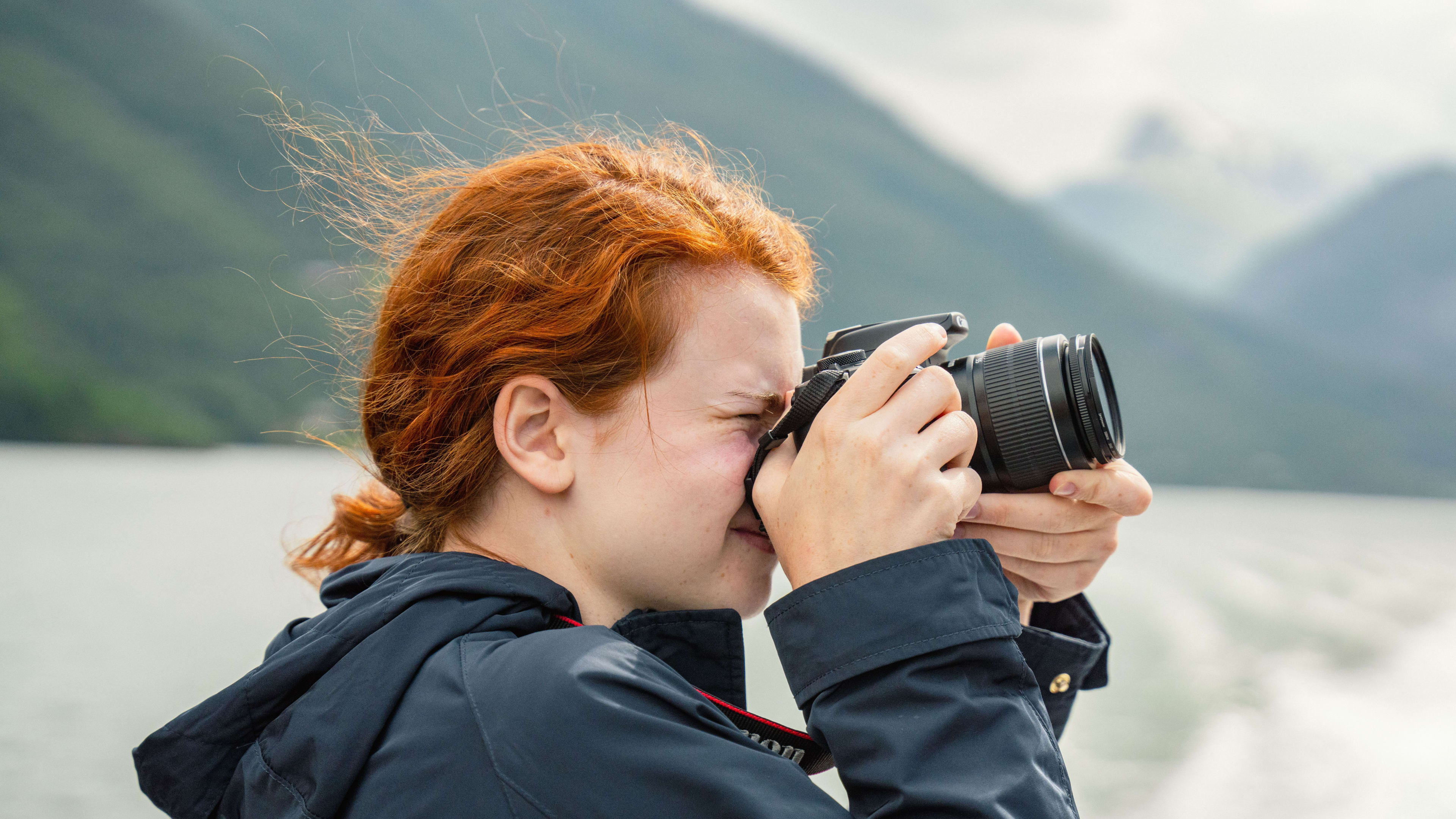Person with red hair photographs misty Sognefjord landscape from boat.