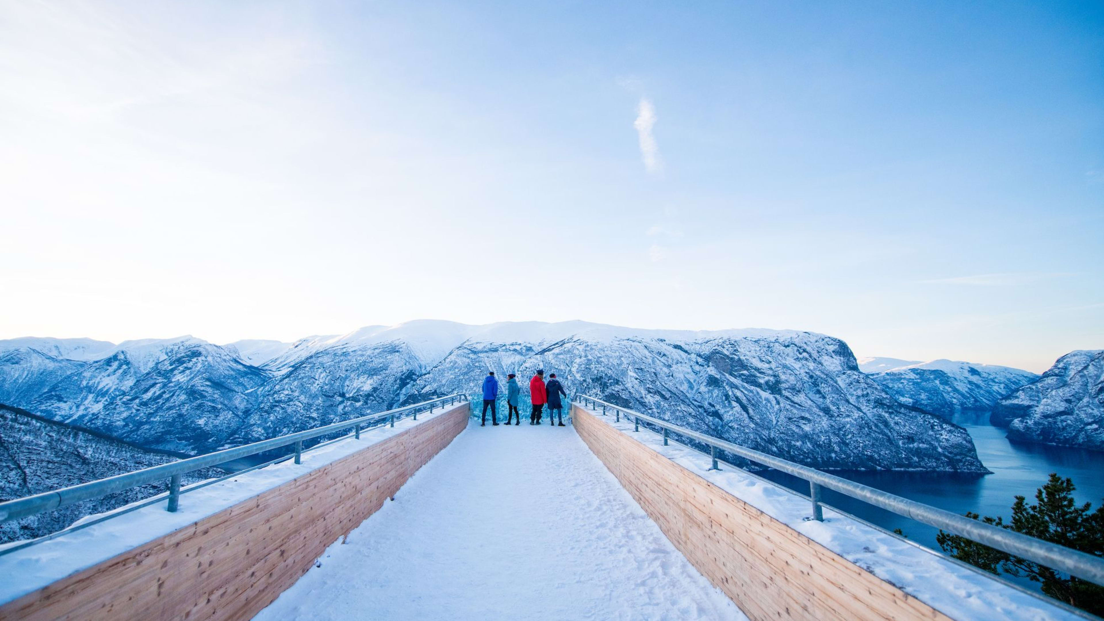 Folk ser utover fjord og snøfjell fra plattform.