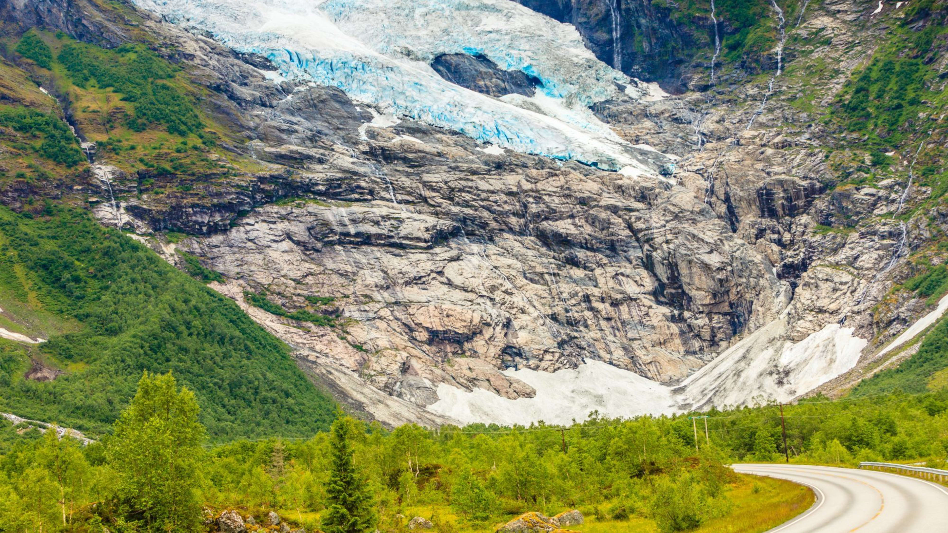 Road winds through valley toward a vast glacier with blue ice.
