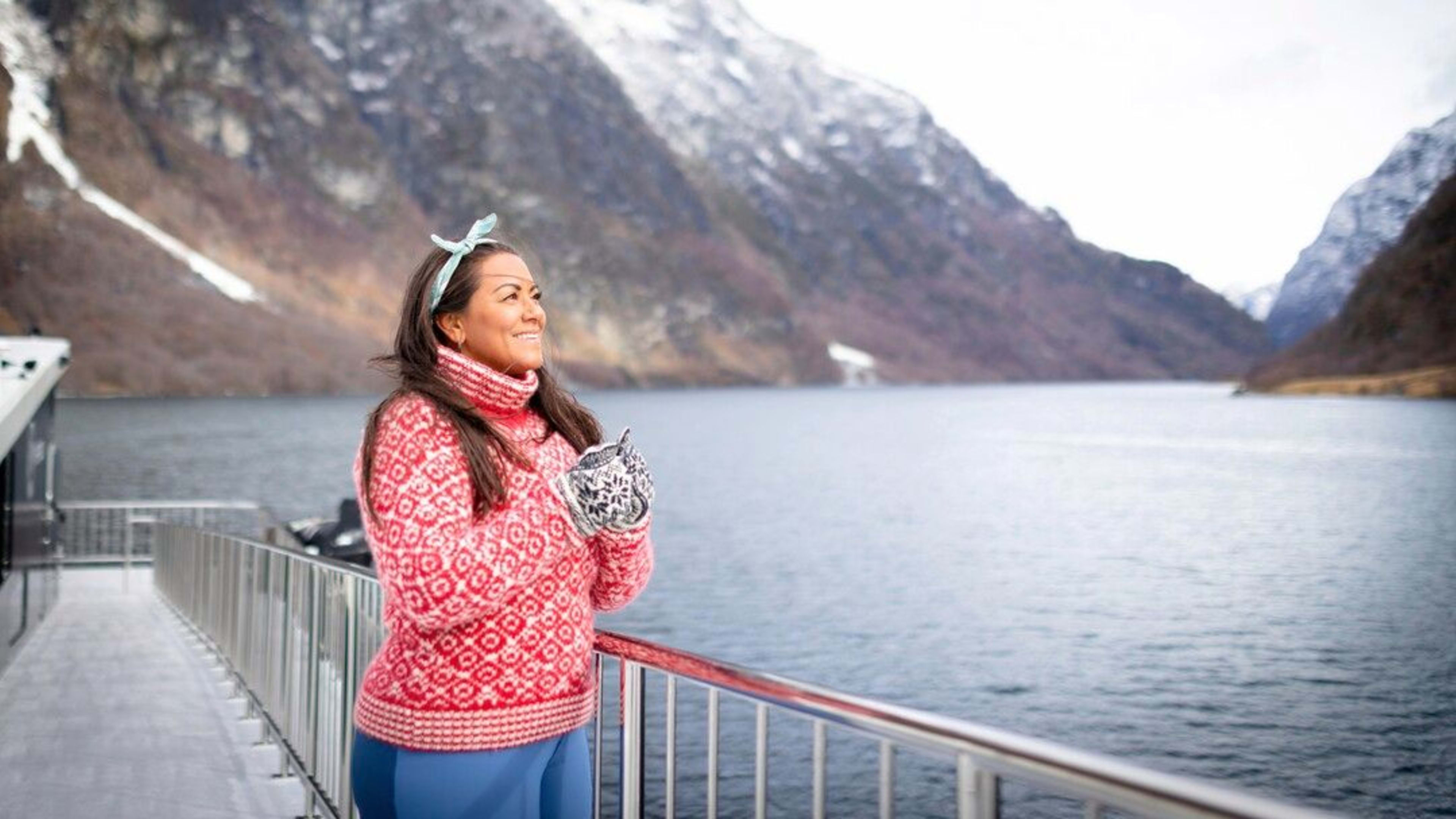 Woman smiles on deck on the fjord cruise at the Nærøyfjord surrounded by snowy fjord and mountains .