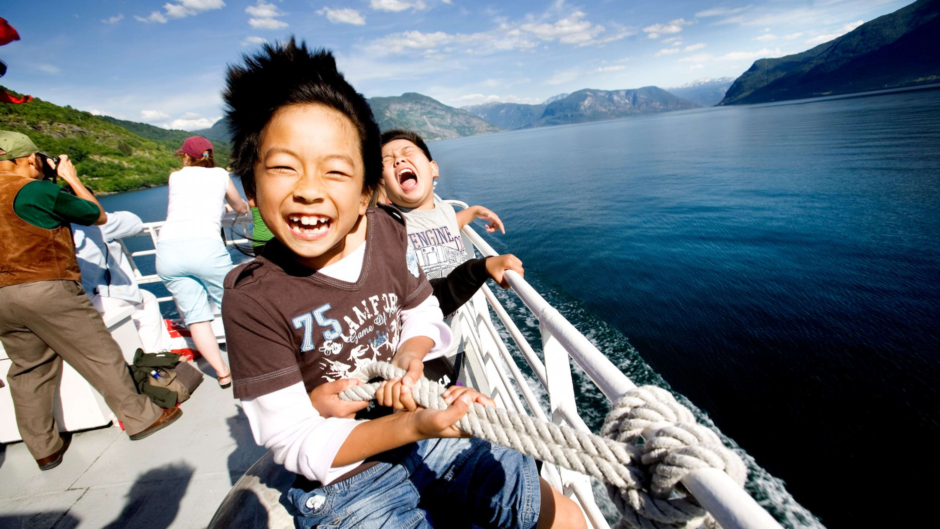 To barn ler og holder i tau på ekspressbåten til Sogn,  blå Sognefjord og skogkledde åser.