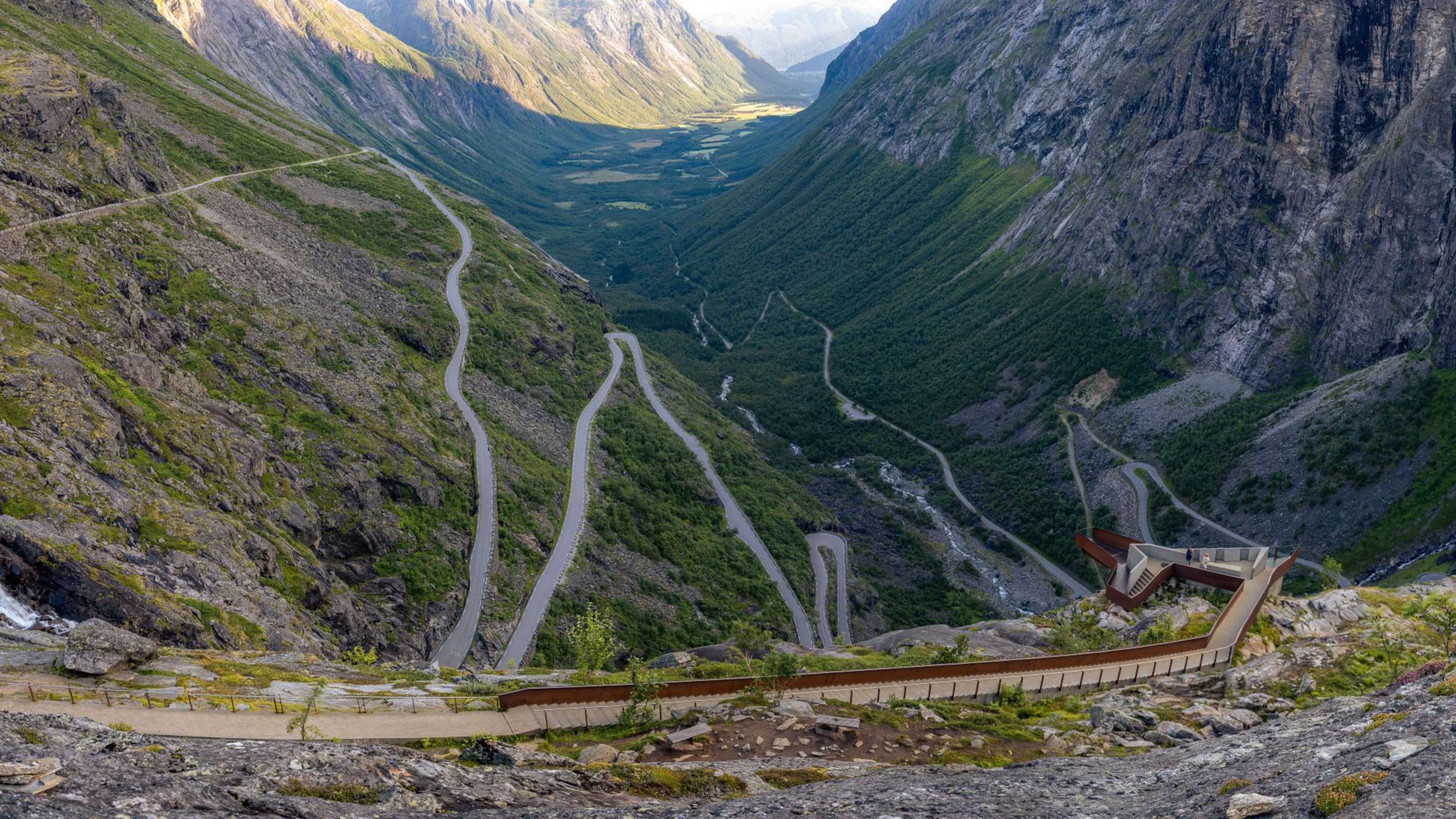Trollstigen veistrekning leder til utsiktsplattform over grønn dal og fjell.