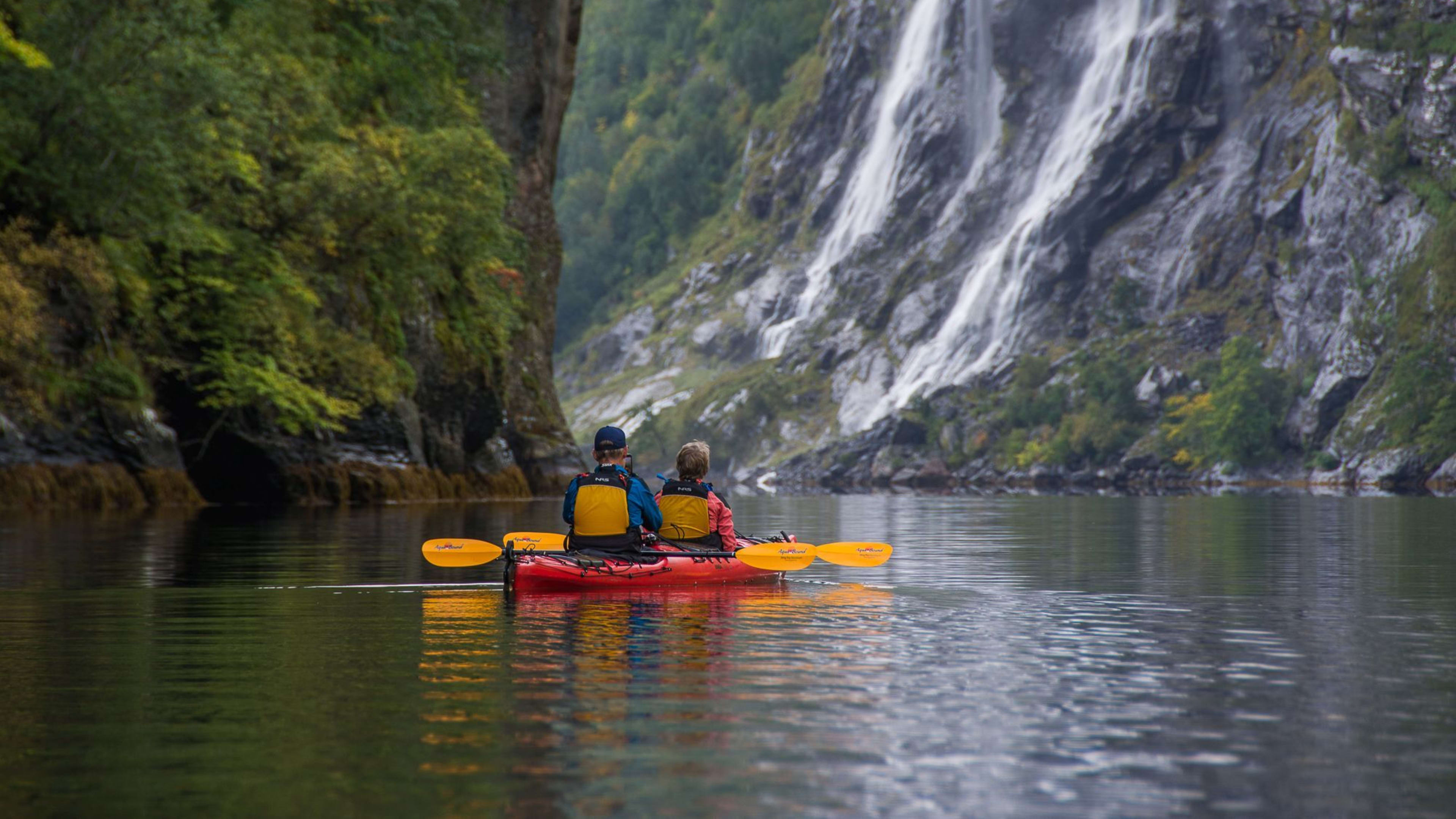 To personer i kajakk nær foss i fjord.