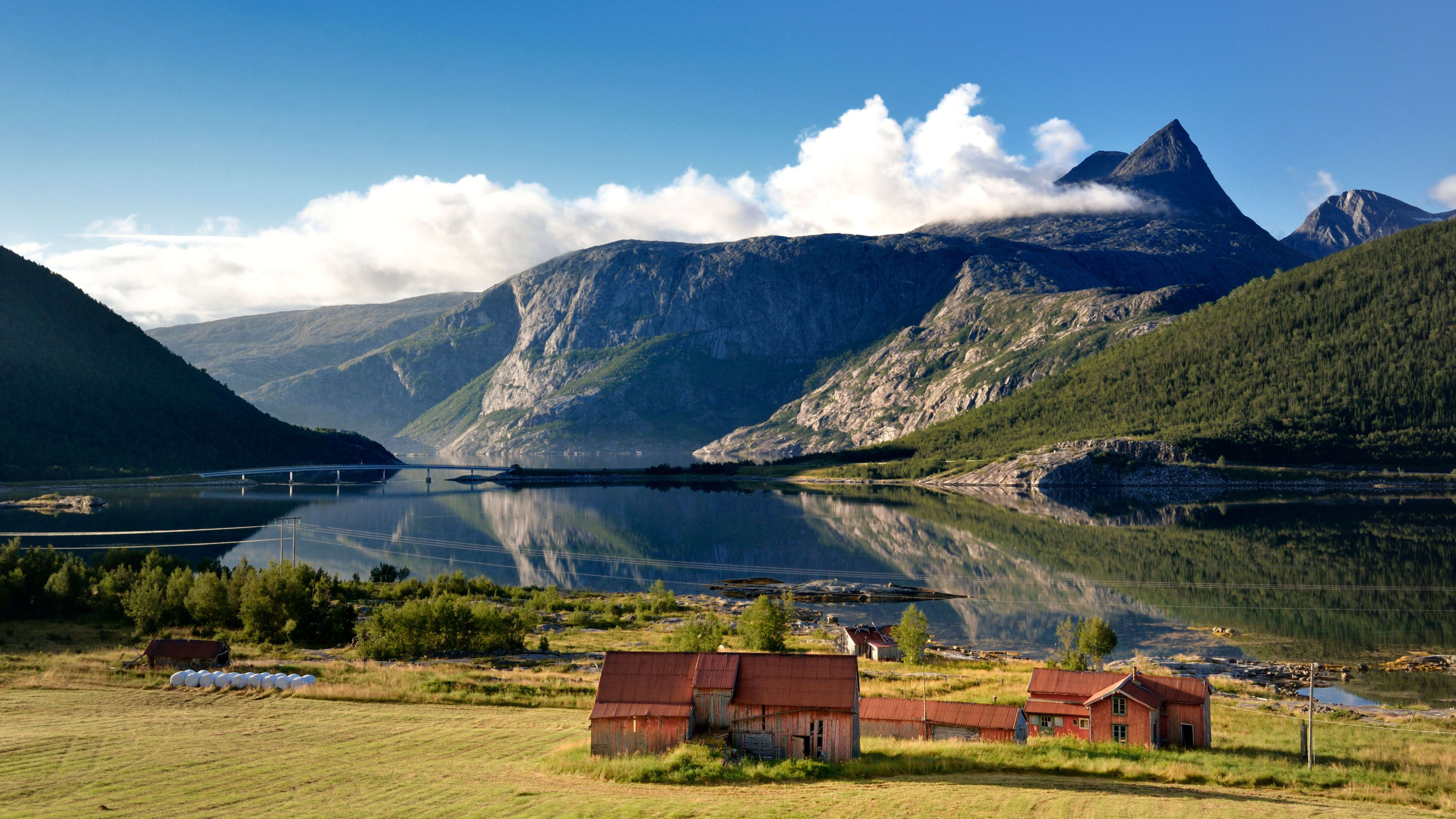 Fargerike hus, frodige marker og fjell speiler seg vakkert i stille fjordvann.