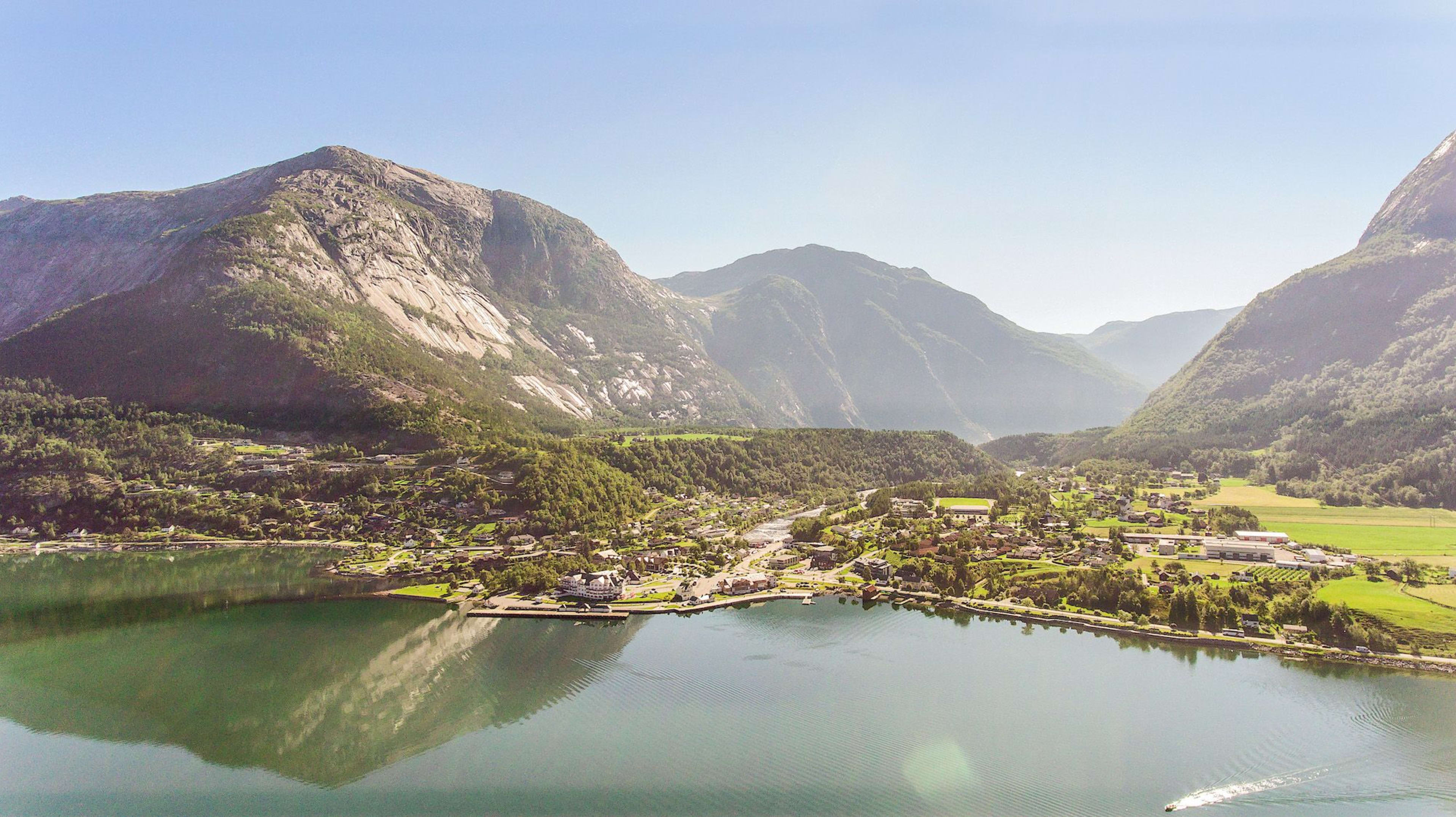 Ruhiges Fjorddorf mit Bootsreflexen und Bergen.