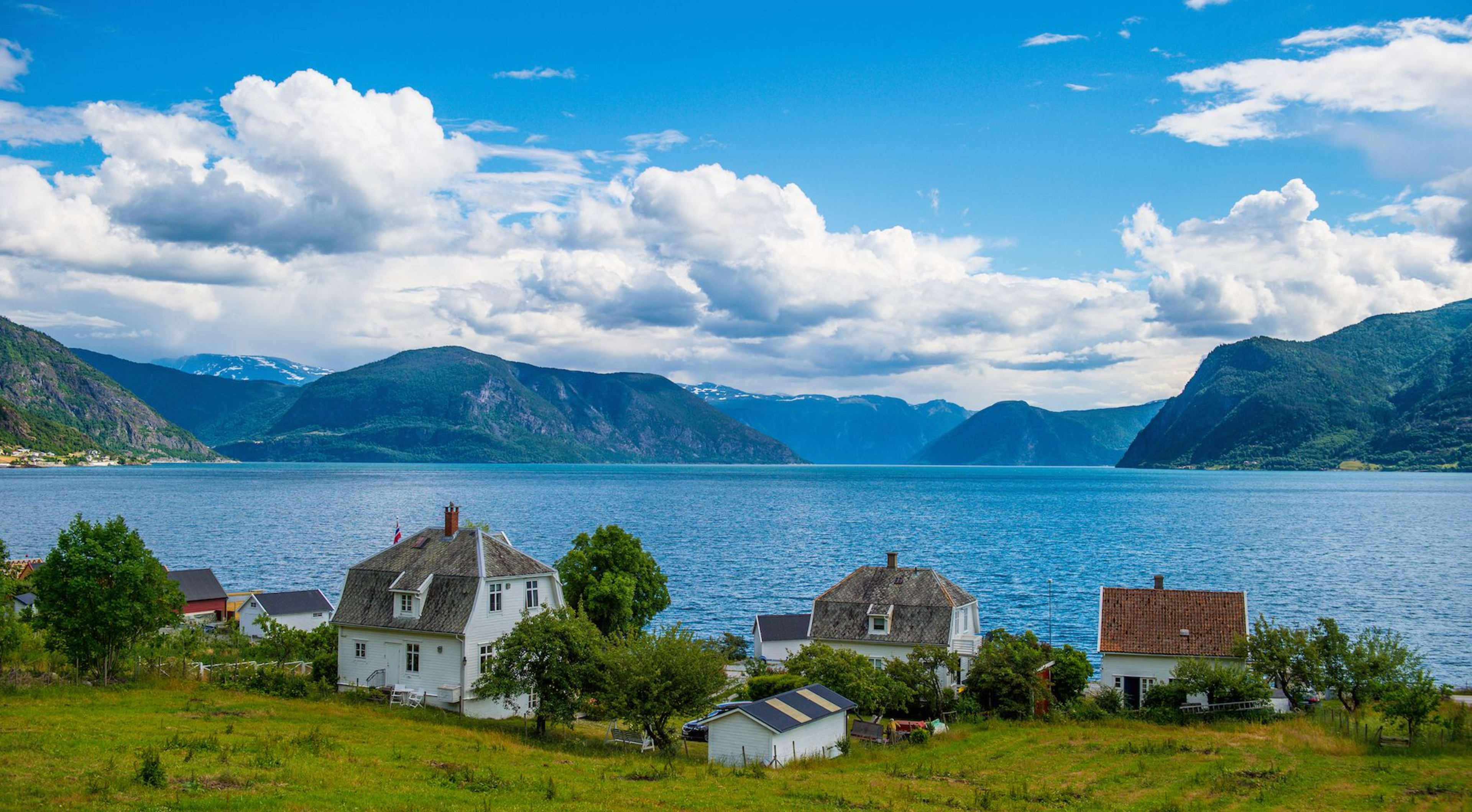 White houses in green fjord village with blue sky and puffy clouds.