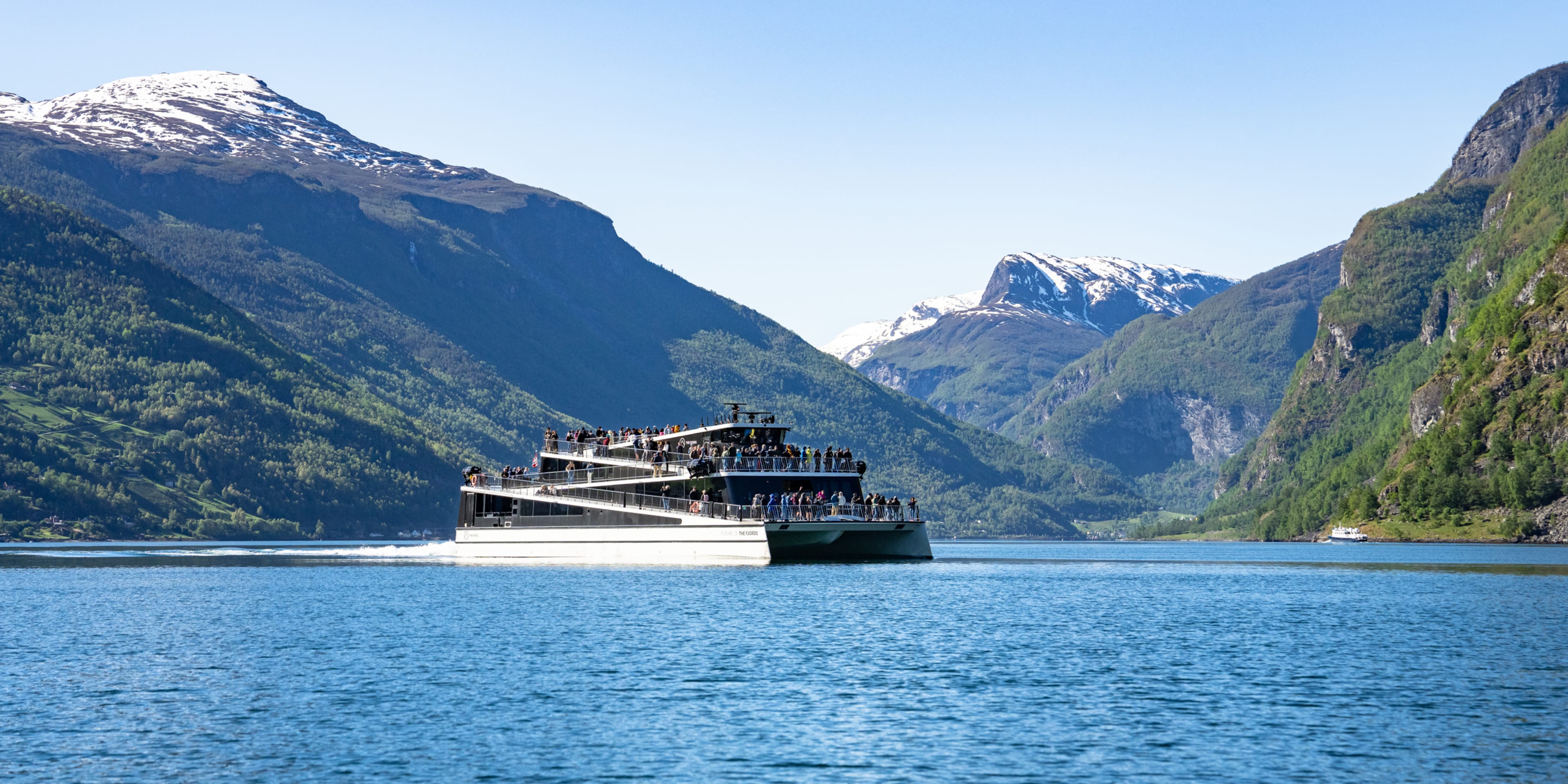 Electric cruise ship sailing through scenic Norwegian fjord with snow-capped mountains