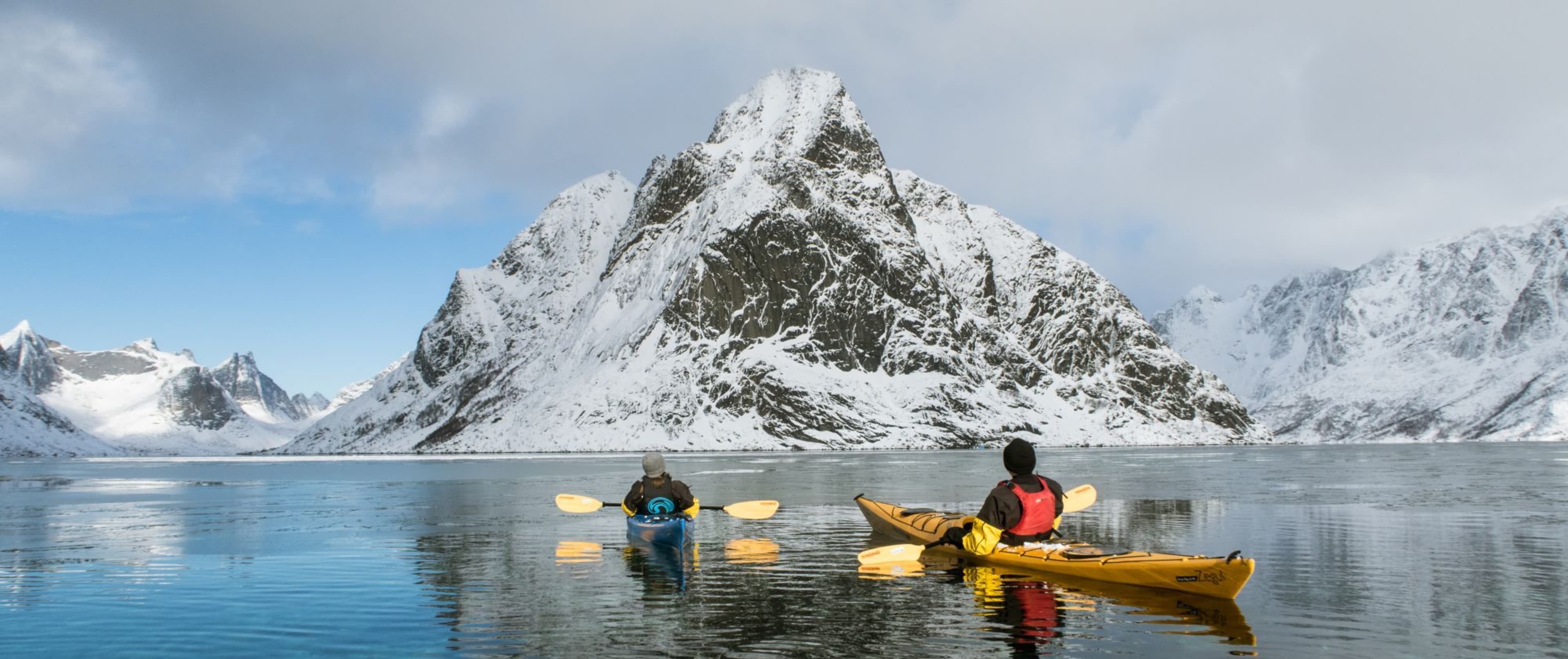 Zwei Kajakfahrer auf eisigem Fjord mit Schneebergen und Sonne.