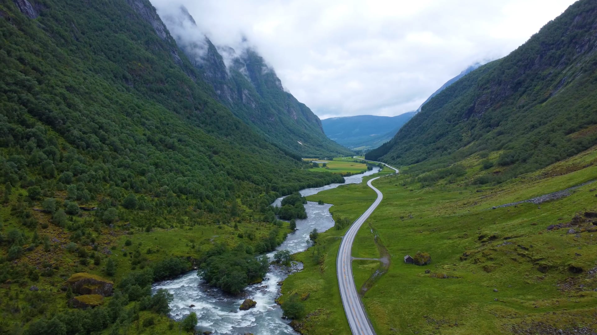 Svingete vei og elv i grønn, tåkekledd fjelldal.