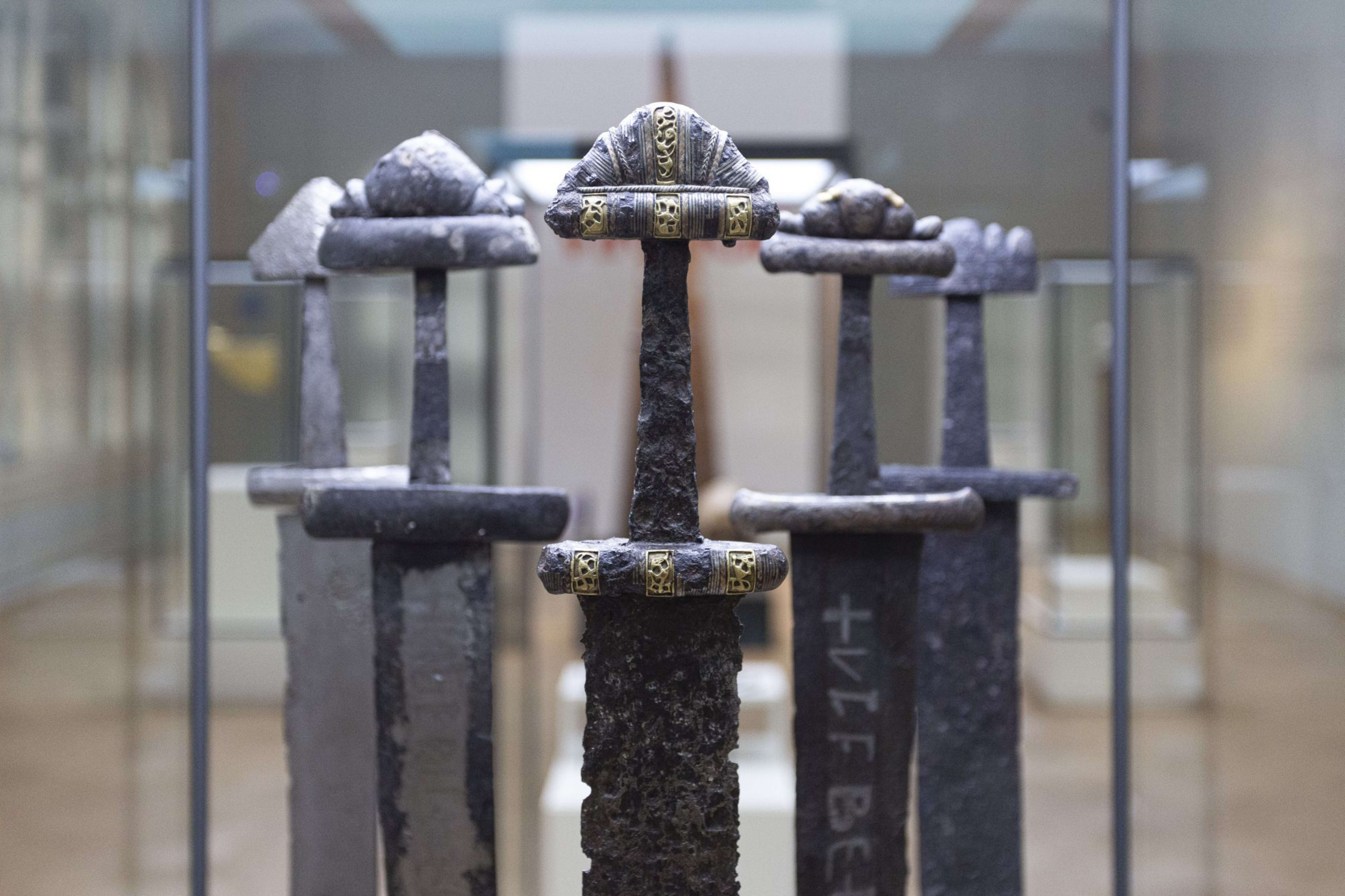 Ancient Viking swords displayed in a museum, focusing on intricate hilts, gold accents, and preserved blades in glass case.