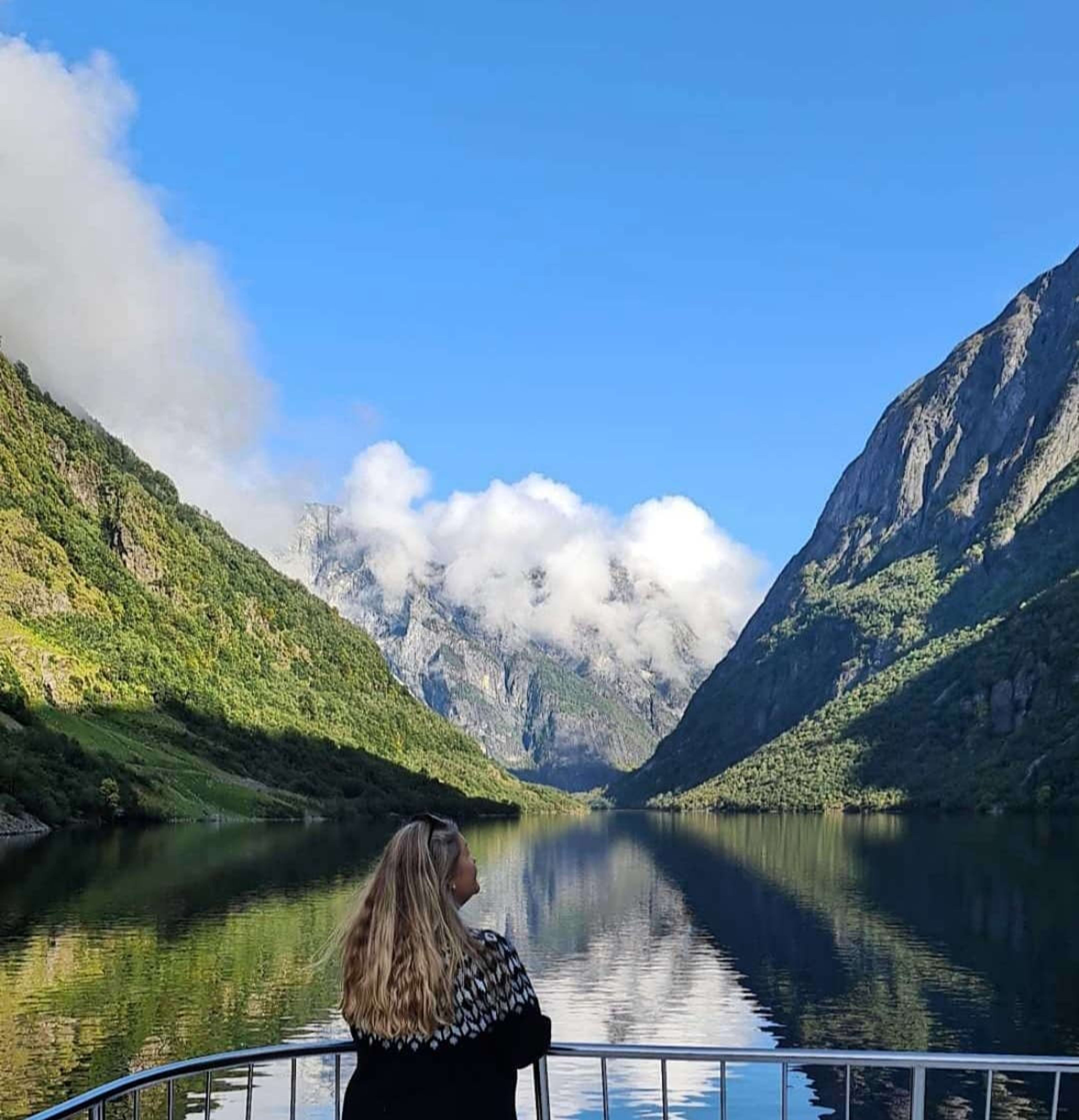 Woman on boat deck admires fjord and steep green mountains.