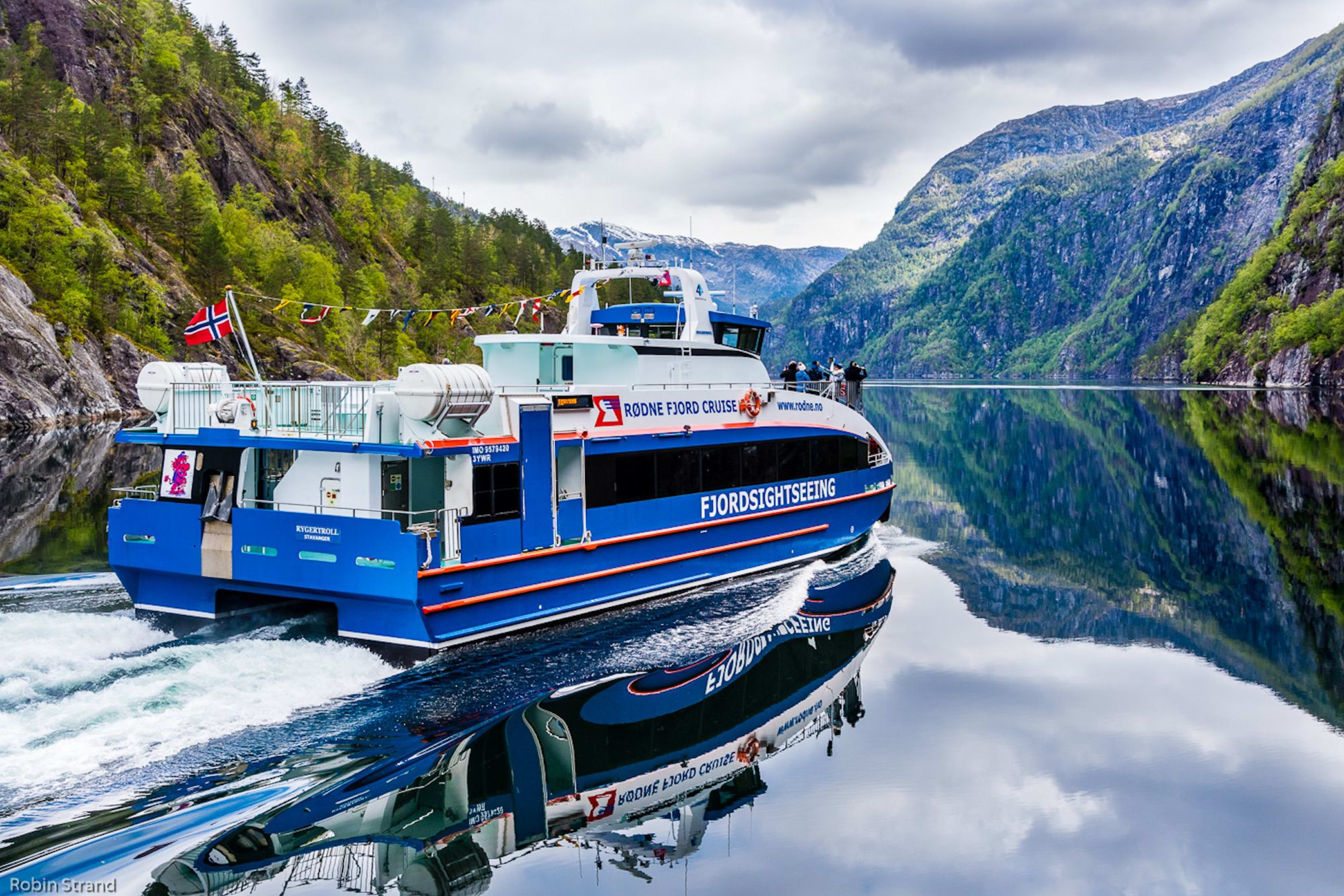 Buntes Fjordboot auf ruhigem Wasser mit Bergspiegelung.