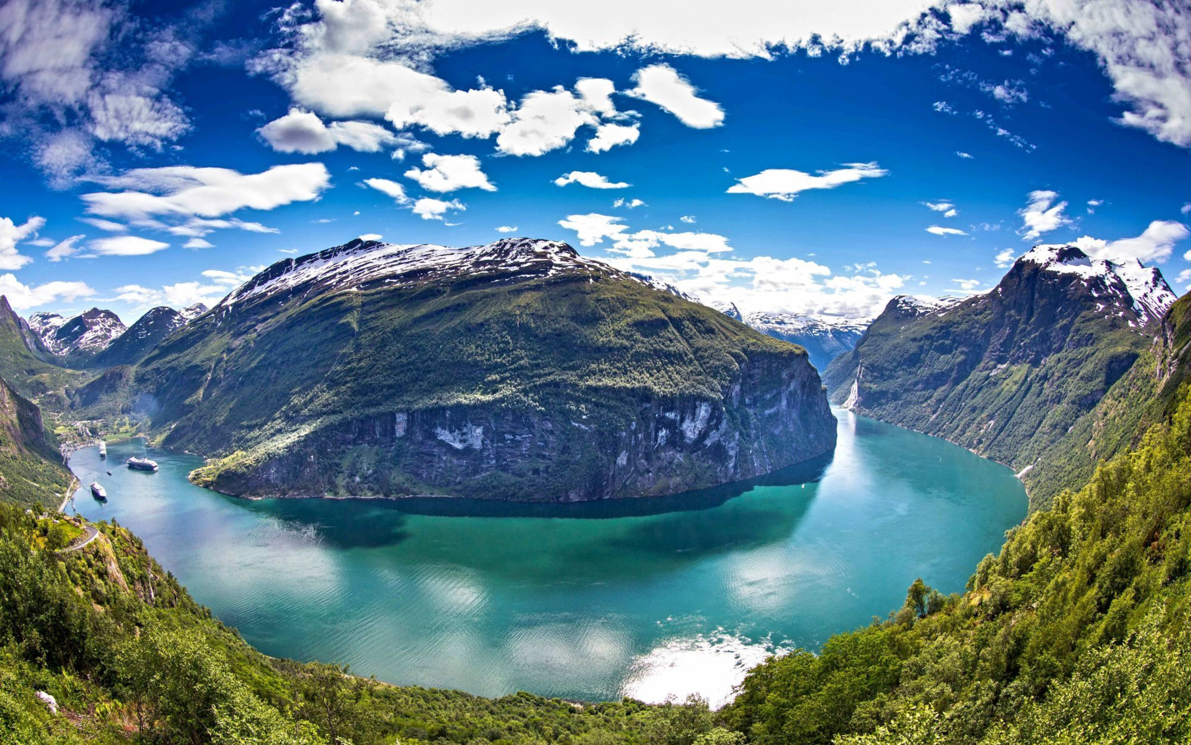 Turquoise fjord with cruise ships, forested mountains and snow.