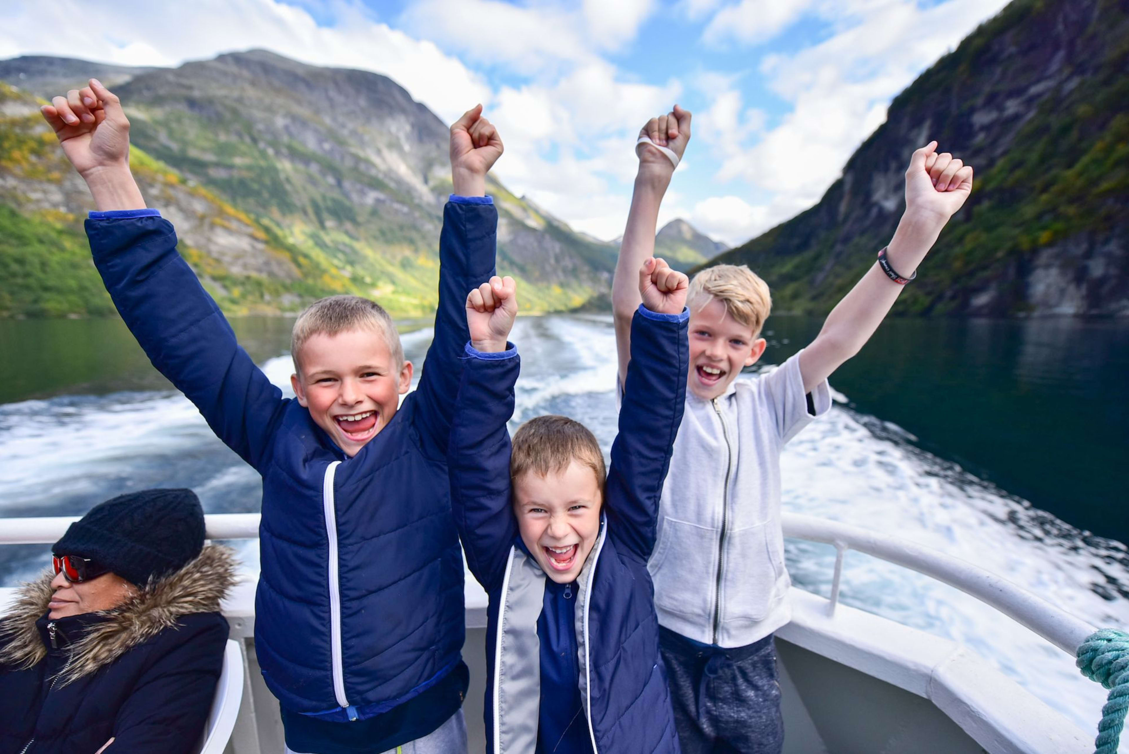 Drei Jungs jubeln an Bord im engen Fjord mit Klippen.