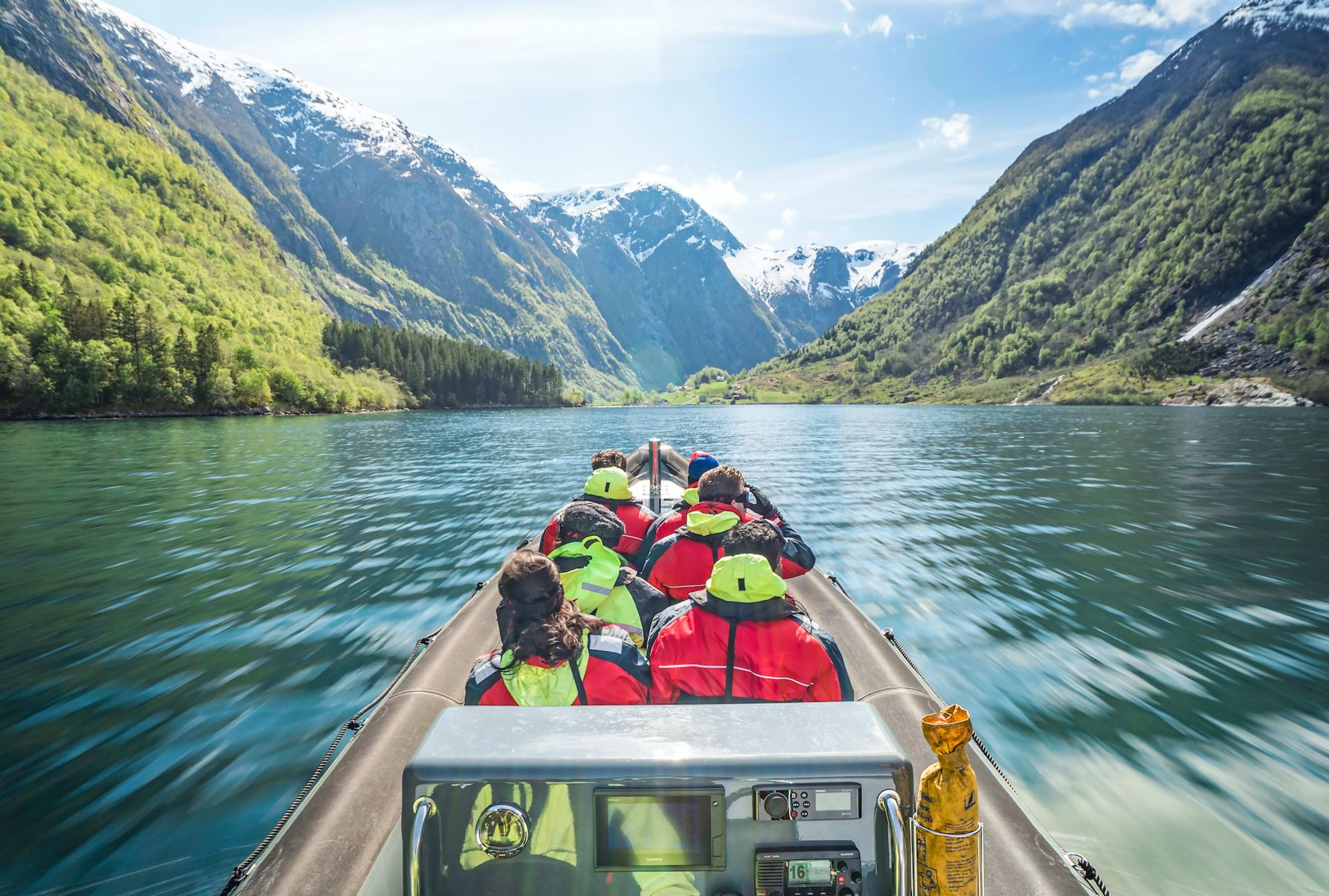 Tourists in safety jackets on RIB  boat ride through turquoise Sognefjord surrounded by lush mountains.