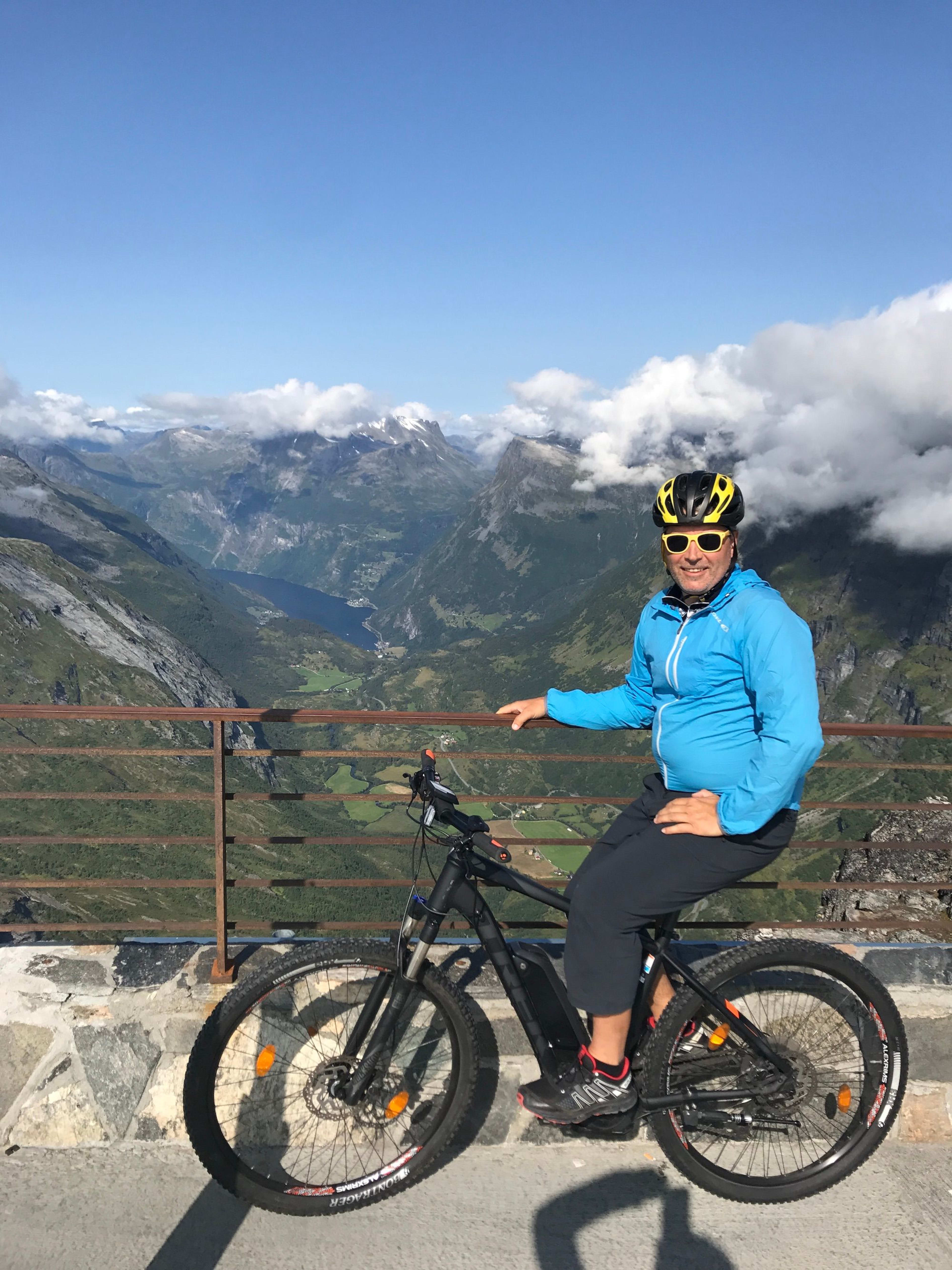 Radfahrer blickt ins grüne Tal mit fernen Bergen.