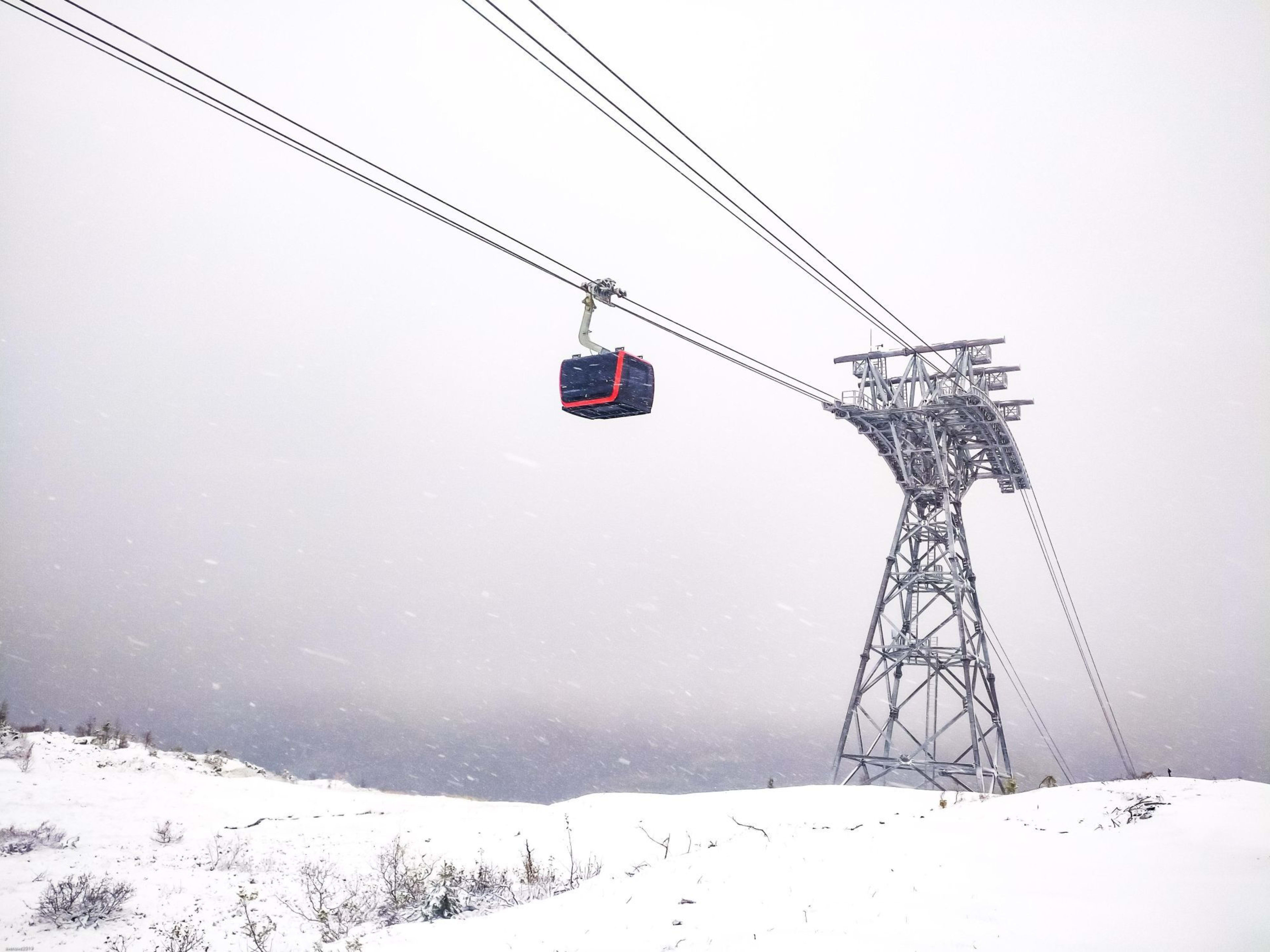 Rød gondol i snøstorm ved tårn, alt er hvitt.