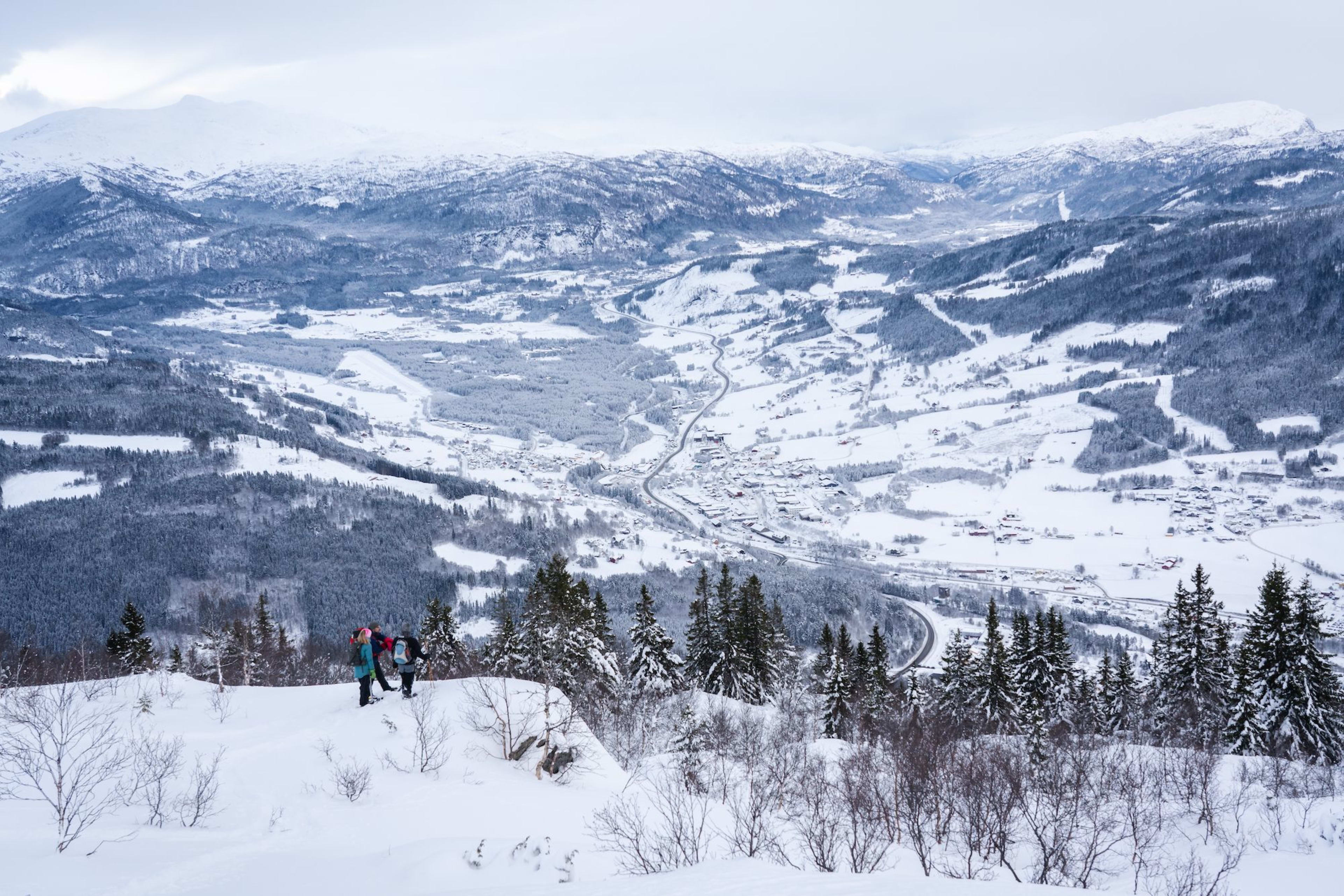 Tre går i snø over dal med fjell.