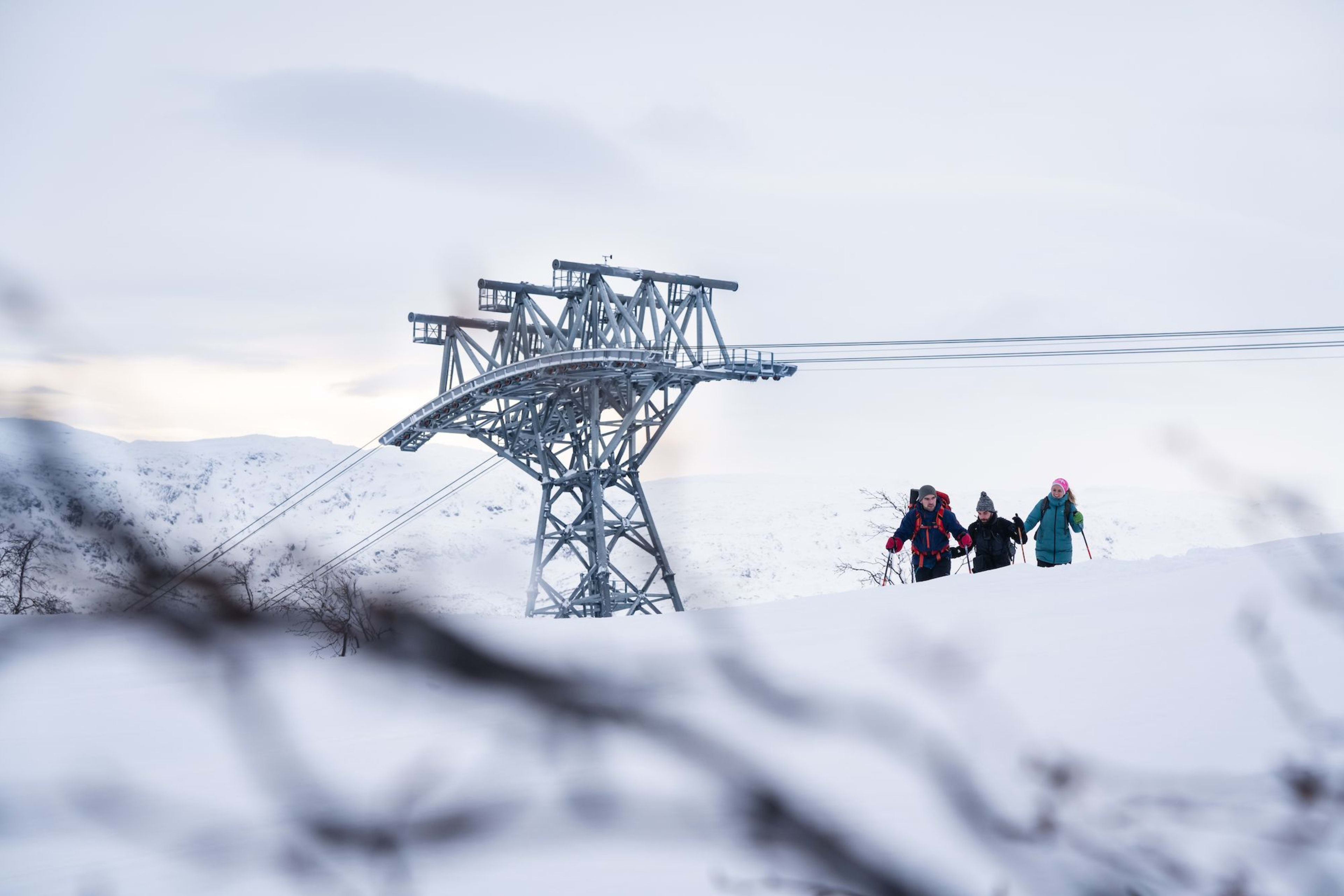 Turgåere i snø nær gondoltårn og fjell.