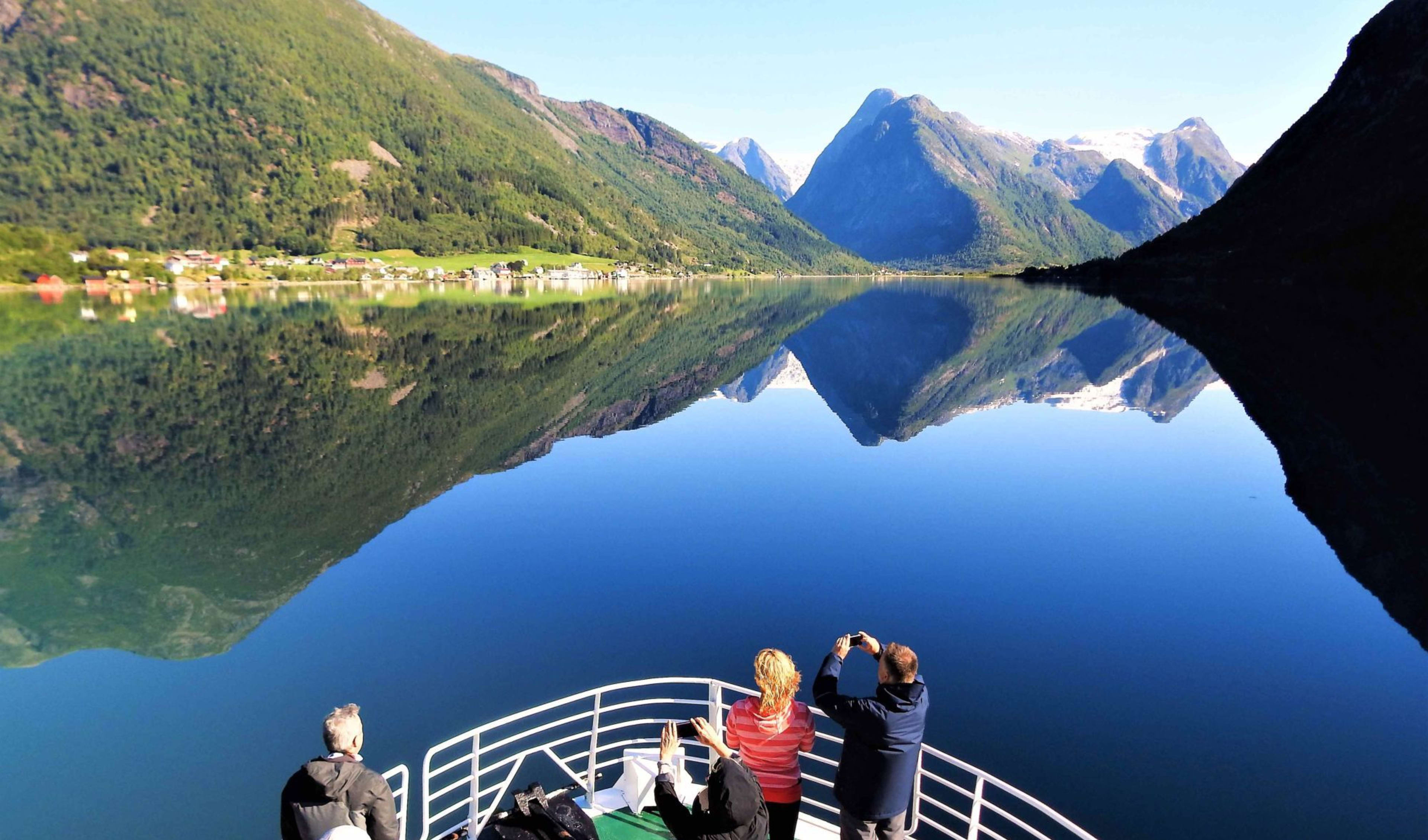 Tourists enjoy a fjord view with mirror-like water and snowy peaks.