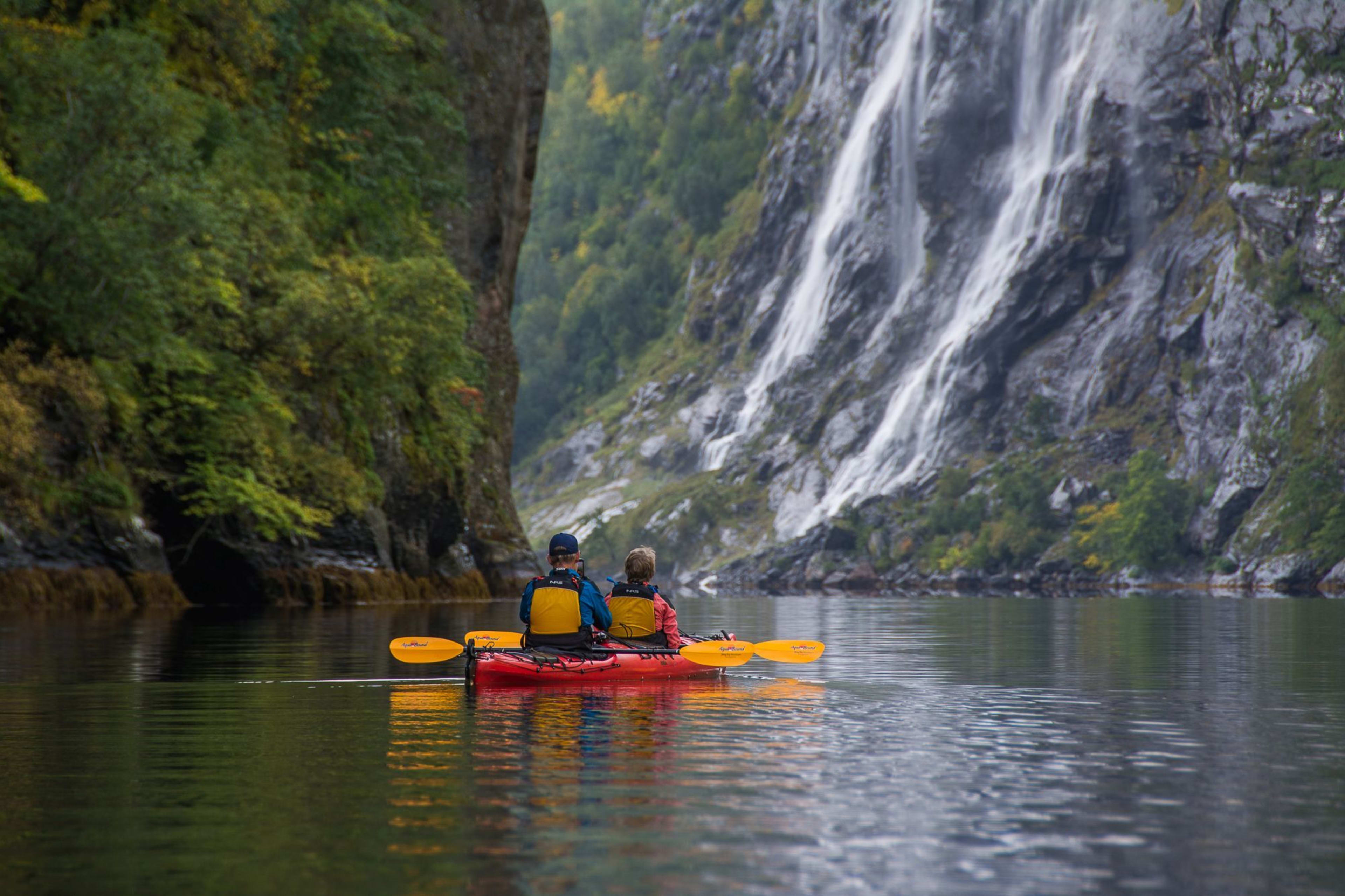 Zwei Personen im Kajak nahe Wasserfall im Fjord.