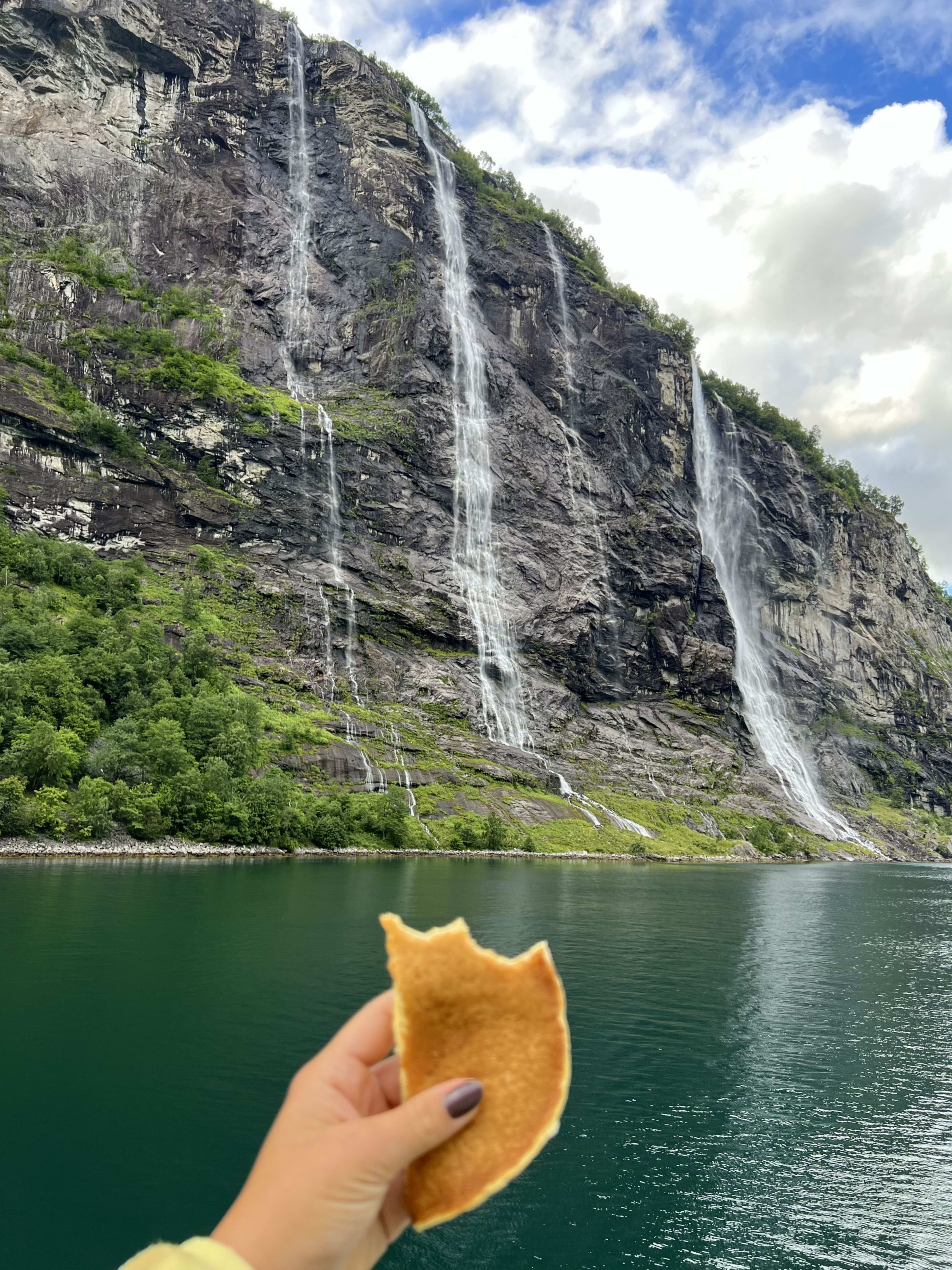 Hand holding pancake with waterfalls in background.