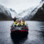 Menschen in leuchtend gelben Thermokombinationen auf einem Boot, lächelnd und posierend für ein Foto auf ruhigem Fjordwasser.