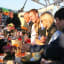 Group of people enjoying drinks on a boat deck, sharing smiles, with wine bottles and glasses, in warm sunlight.