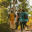 Three hikers with backpacks walking rocky trail in sunny forest, sunlight casting shadows.