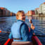 Frau genießt Eis auf geführter Kajaktour in Trondheim vorbei an bunten Gebäuden am Wasser an sonnigem Sommertag