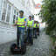 Menschen auf Segways fahren durch eine enge Kopfsteinpflastergasse mit weißen Holzhäusern.