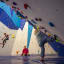 A group of children participating in indoor rock climbing, with colorful handholds and a climbing wall.