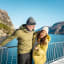 Smilende par som nyter fjordcruise på Lysefjorden om vinteren, med fjord og fjell i bakgrunnen.