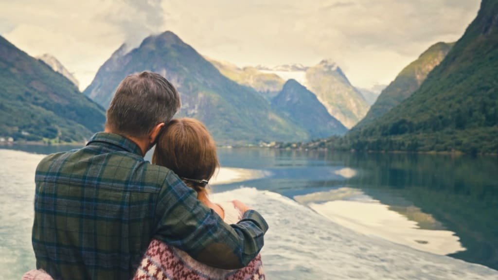 Par omfavner hverandre og ser ut over Sognefjorden og skyer i vannet.