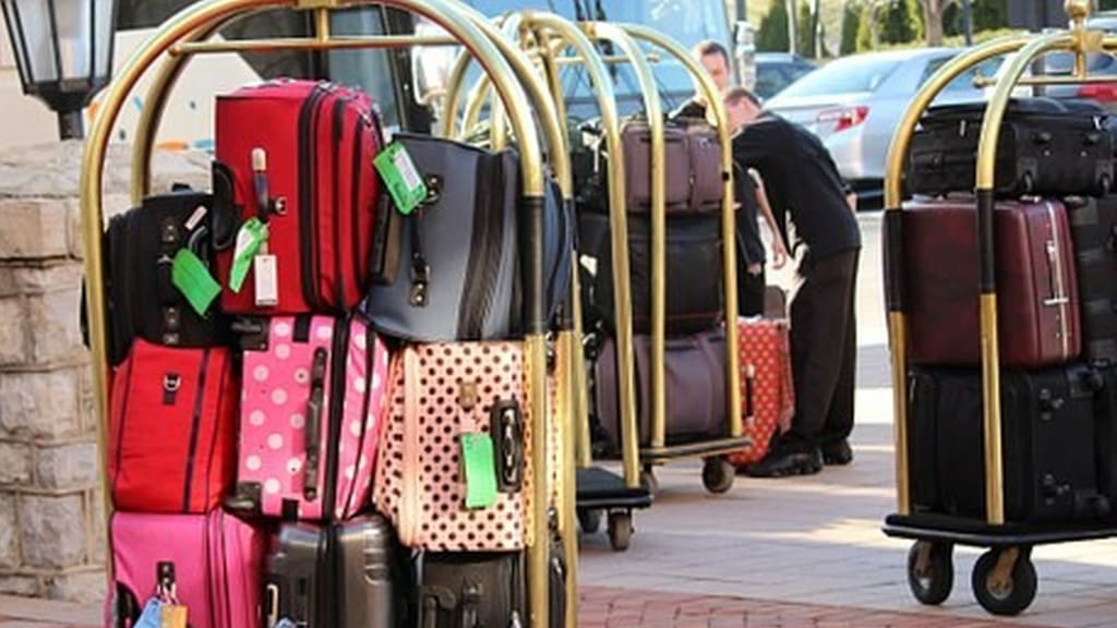 Colorful suitcases stacked on hotel luggage carts, hotel worker arranging bags near cars.