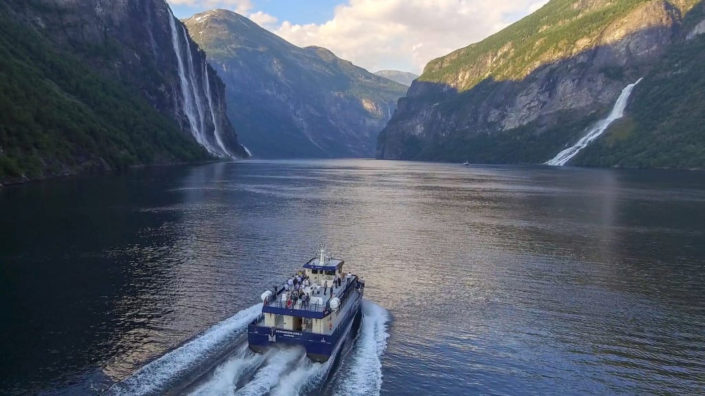 Båttur i Geirangerfjorden omgitt av klipper, fosser og grønne fjell.