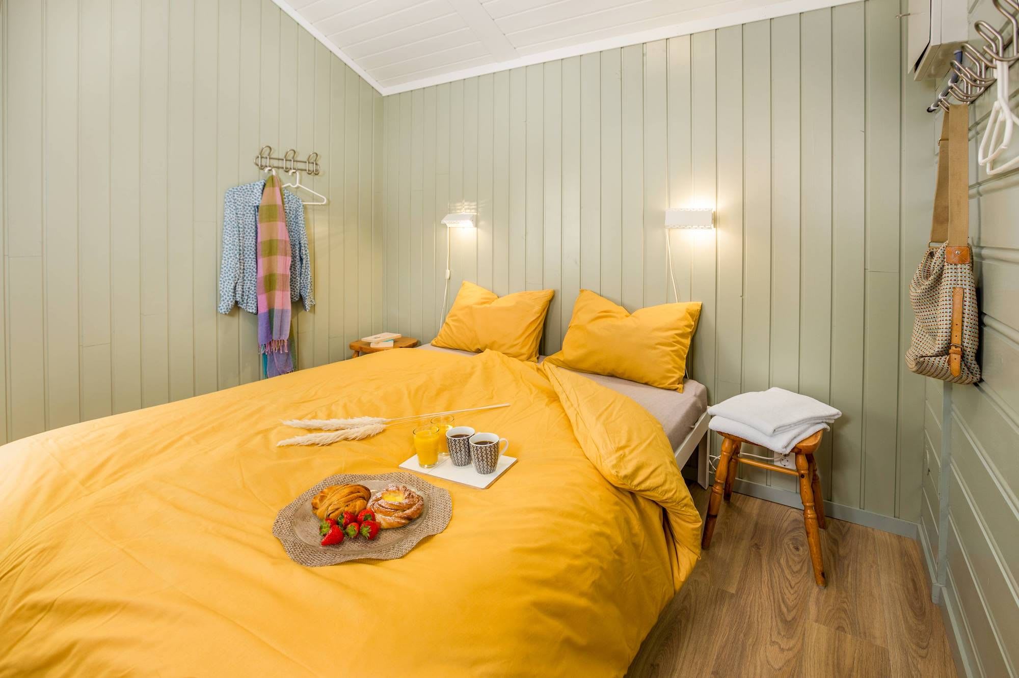Yellow double room in Flåm Camping with green walls and tray with coffee, buns and strawberries