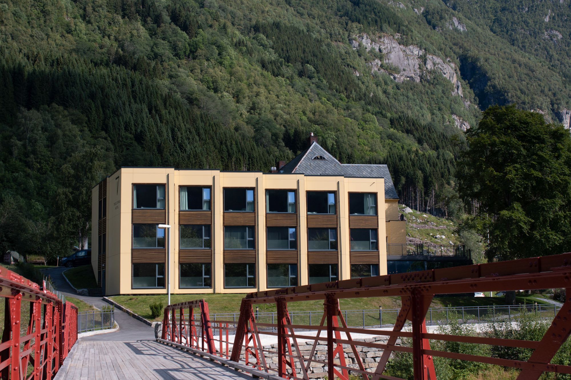 Trolltunga Hotel exterior in Odda with dramatic Norwegian mountains backdrop and scenic bridge over cascading river waterfall