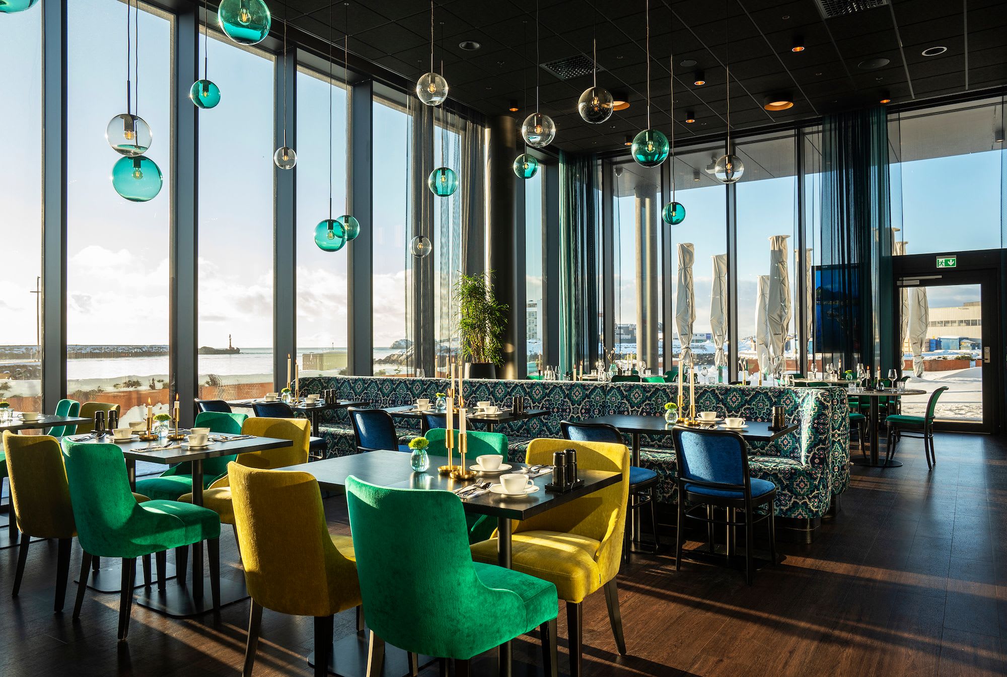 Thon Hotel Svolvær breakfast room with colorful chairs, green pendant lamps and panoramic Lofoten fjord mountain views
