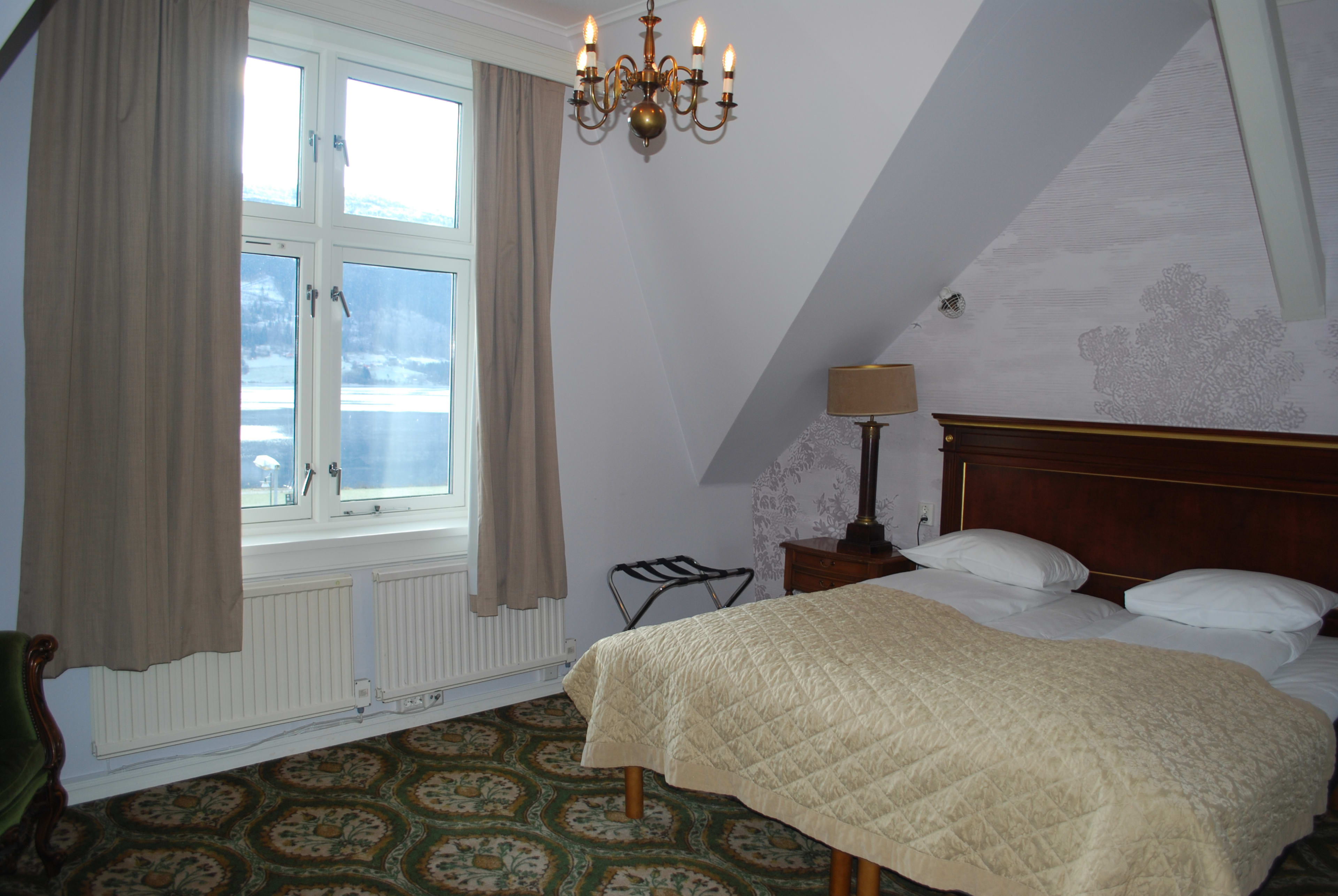 Klassisk dobbeltrom med kingsize-seng og blomstrete tapet på Fleischer's Hotel på Voss med elegant historisk innredning