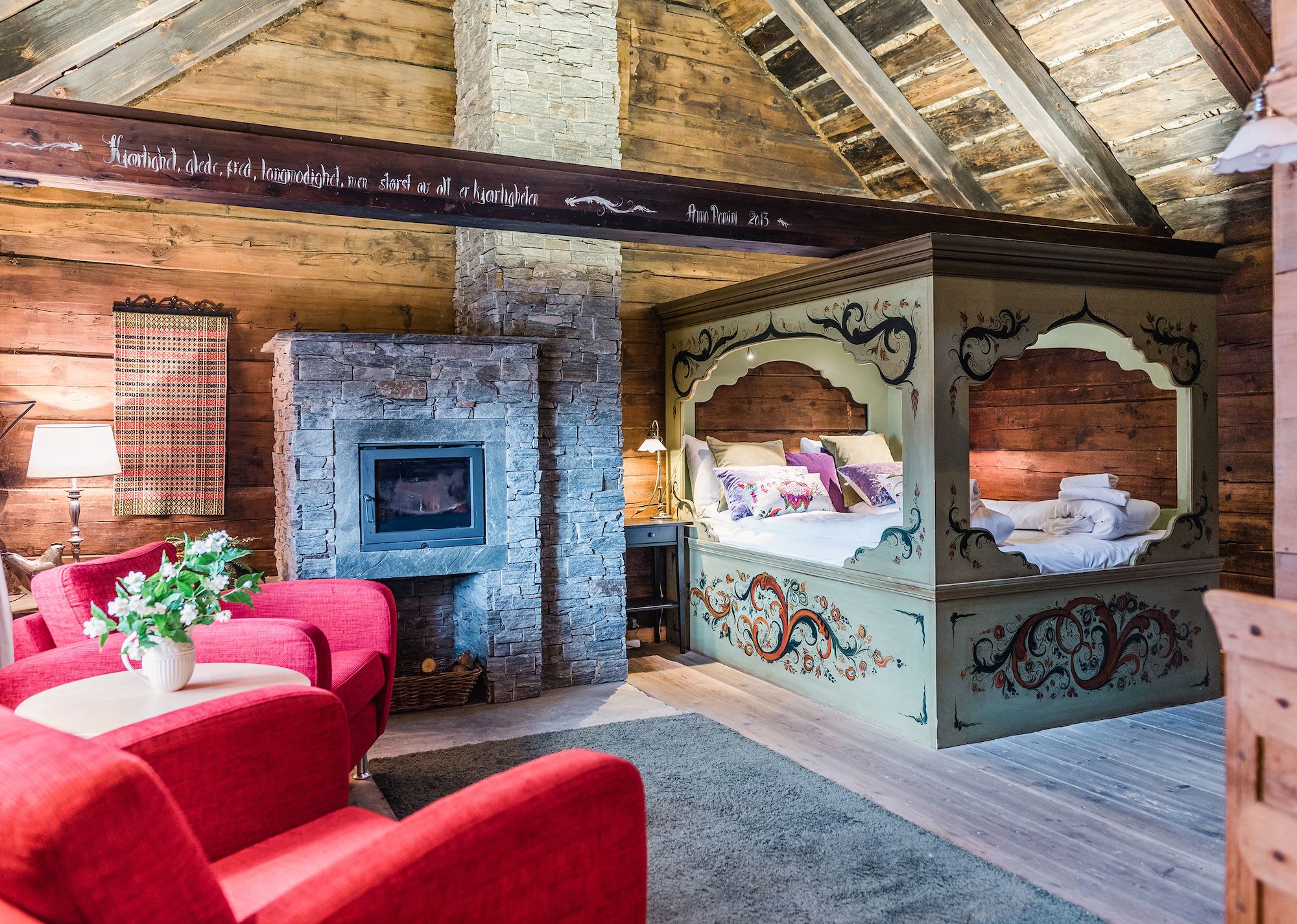 Eldhuset-rommet på Store Ringheim Hotell Voss - tradisjonell utskåret dobbeltseng med rosemaling, steinpeis og røde stoler